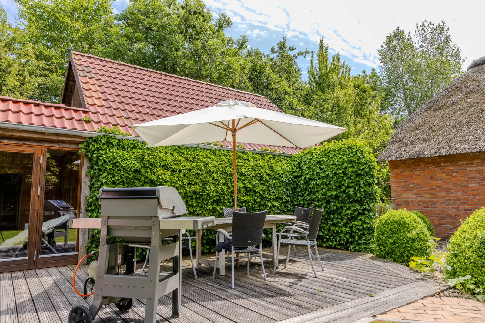 Holzterrasse mit Grill, Sonnenschirm und Gartenmöbeln vor dem Nebengebäude