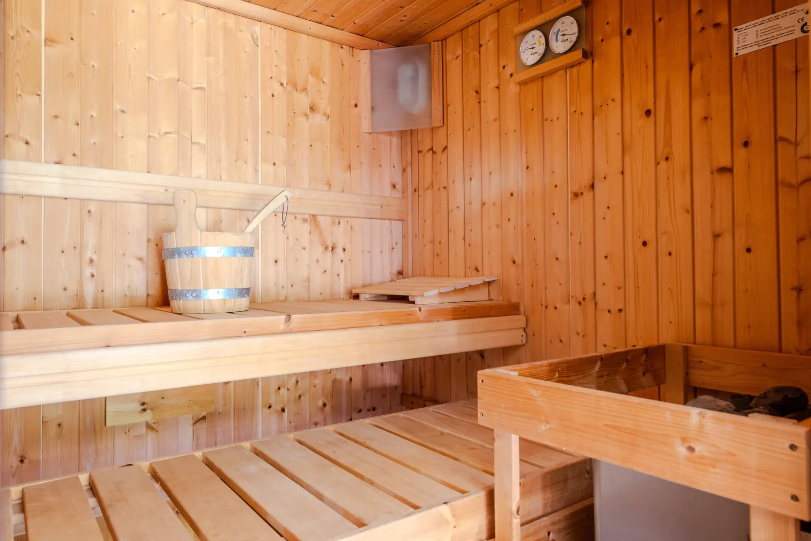 Sauna mit hellen Holzbänken, Saunaeimer und Thermometer