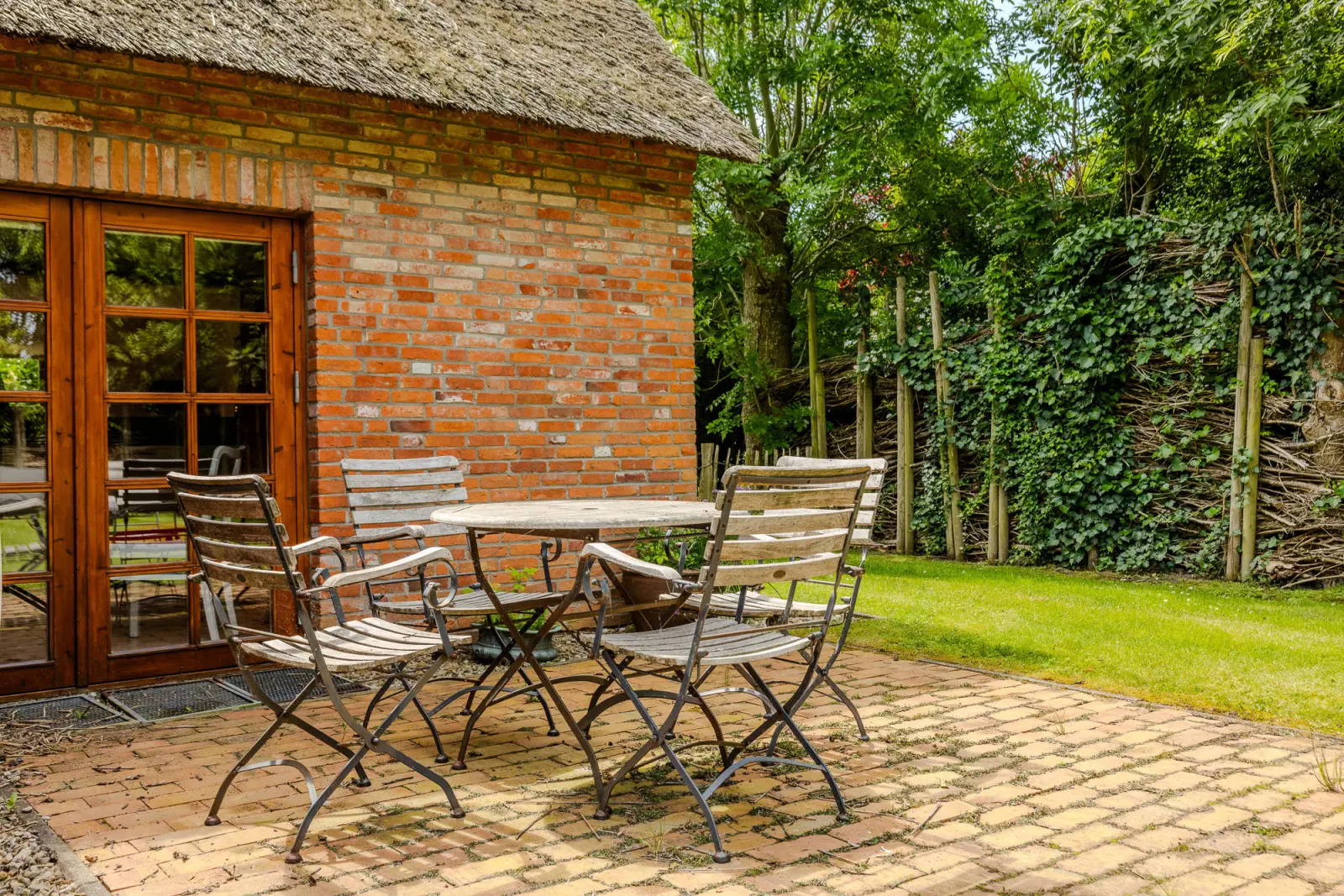 Gartenstühle und Tisch auf gepflastertem Sitzplatz vor der Backsteinwand