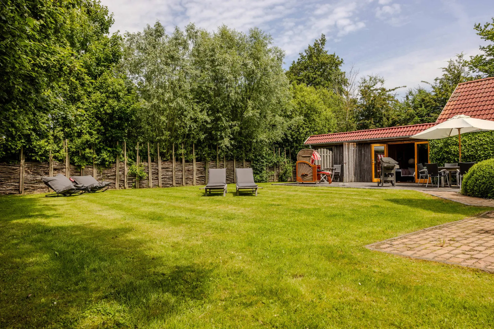 Weitläufiger Garten mit Liegen auf dem Rasen und Nebengebäude mit Terrasse im Hintergrund