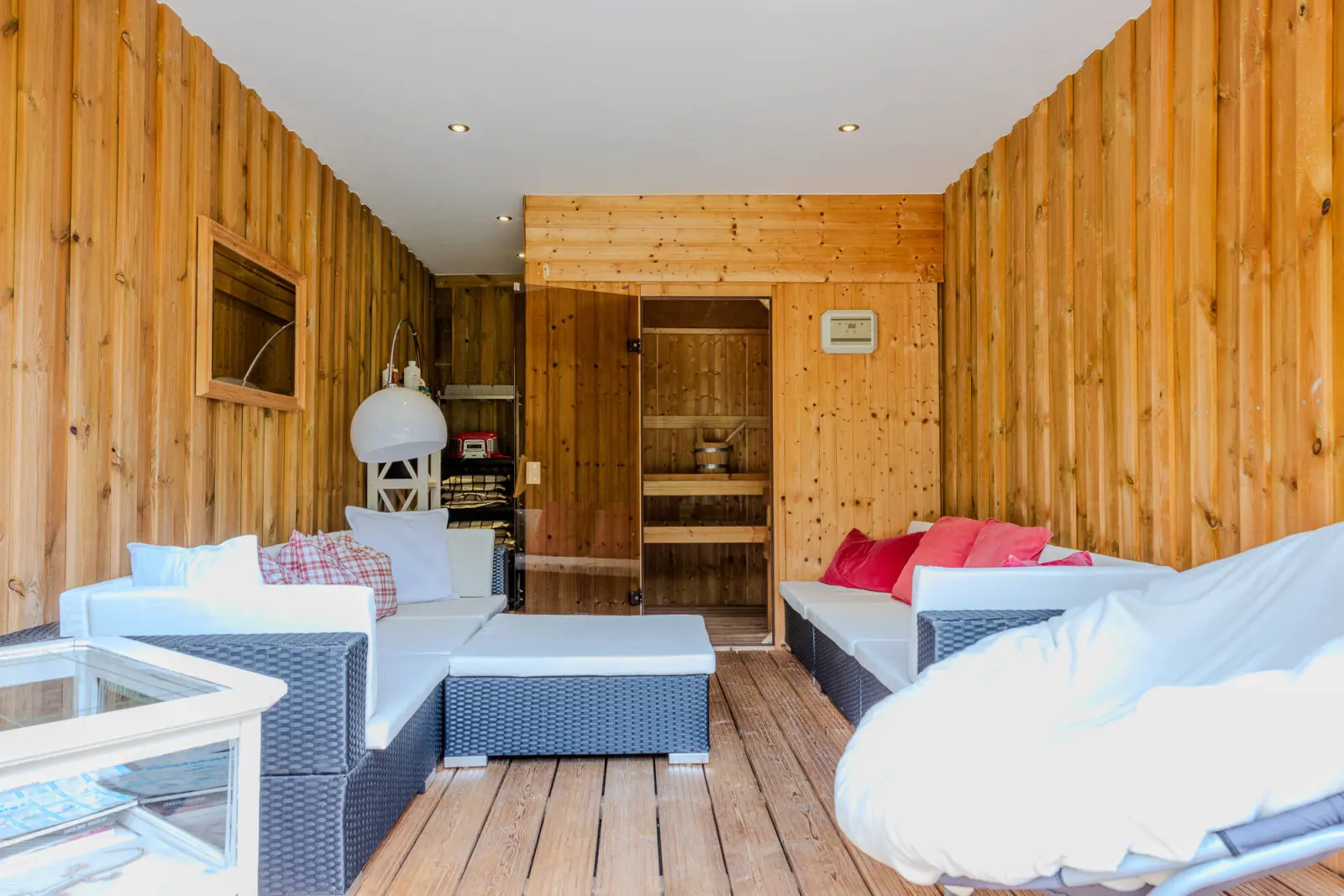 Überdachter Saunabereich mit Rattan-Lounge, Kissen und Saunatür