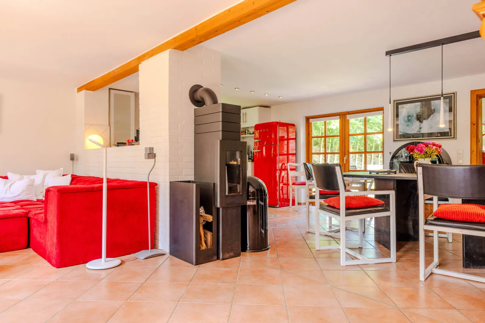 Wohnbereich mit rotem Sofa, Kaminofen und Esstisch im Hintergrund
