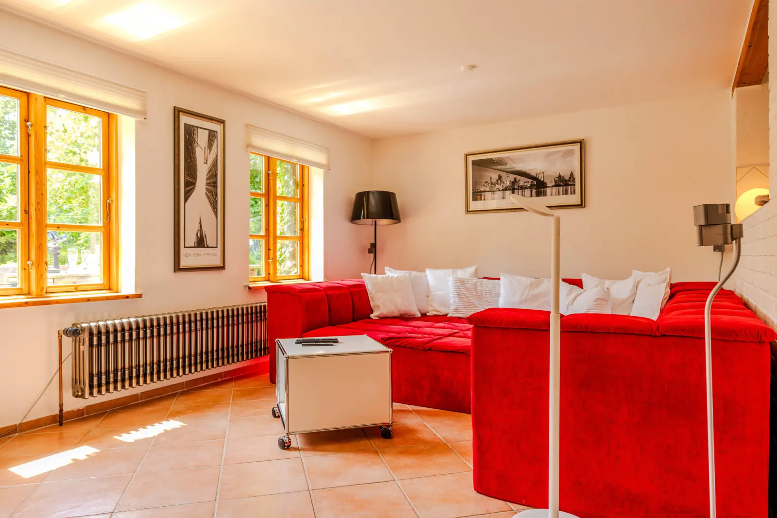 Wohnzimmer mit rotem Ecksofa, Stehleuchte und Terrakottafliesen