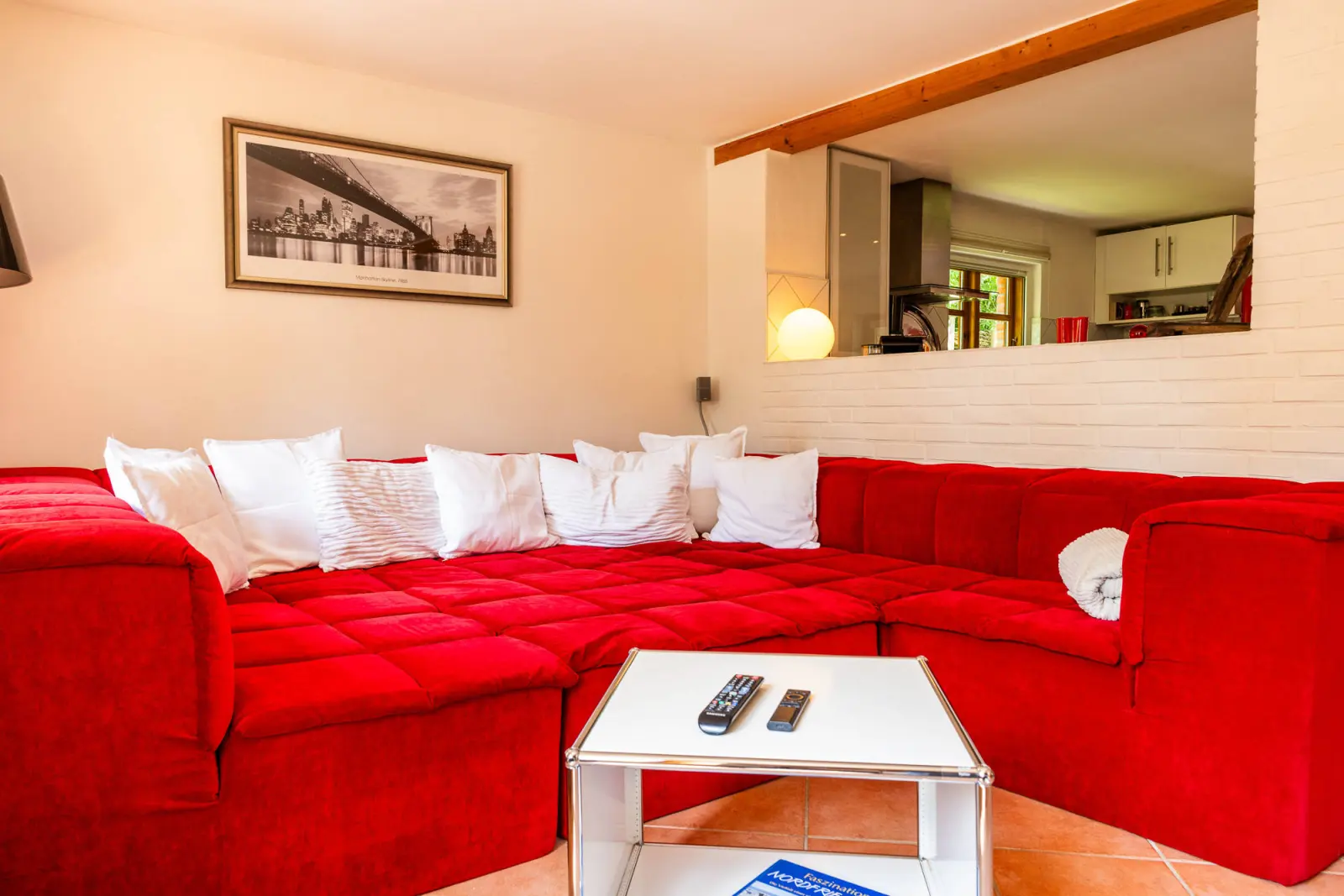Rotes Ecksofa mit weißen Kissen und rollbarem Couchtisch, Durchblick zur Küche