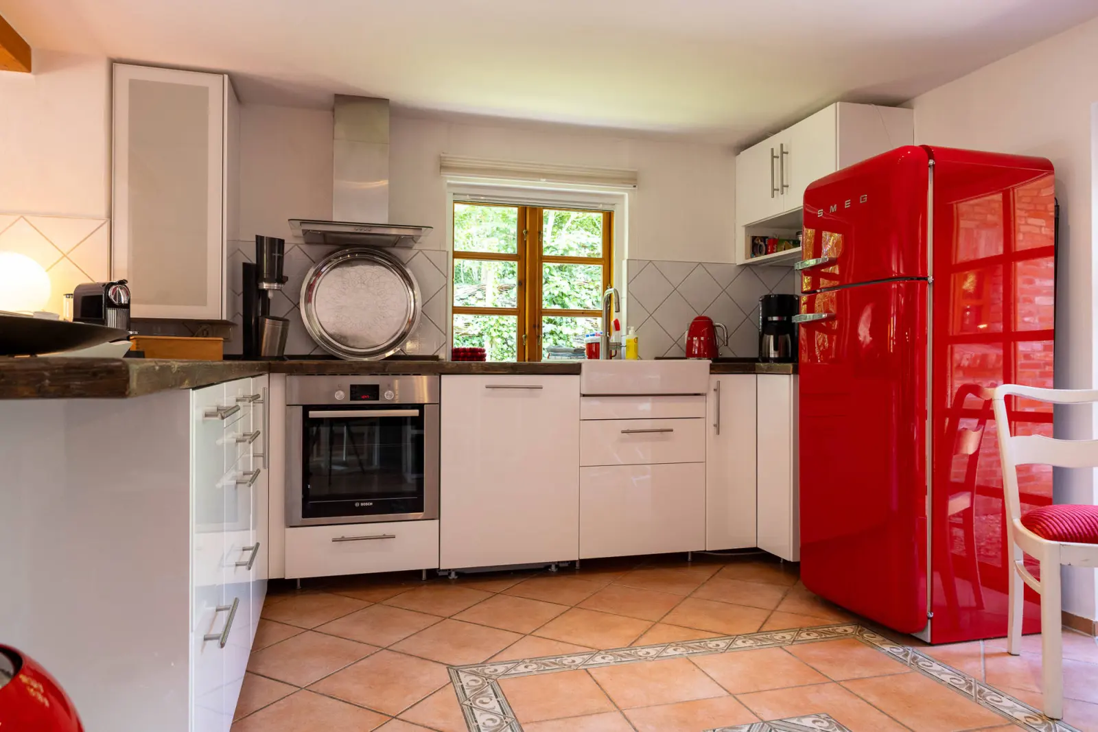 Küche mit weißen Fronten, rotem Retro-Kühlschrank und Terrakottafliesen
