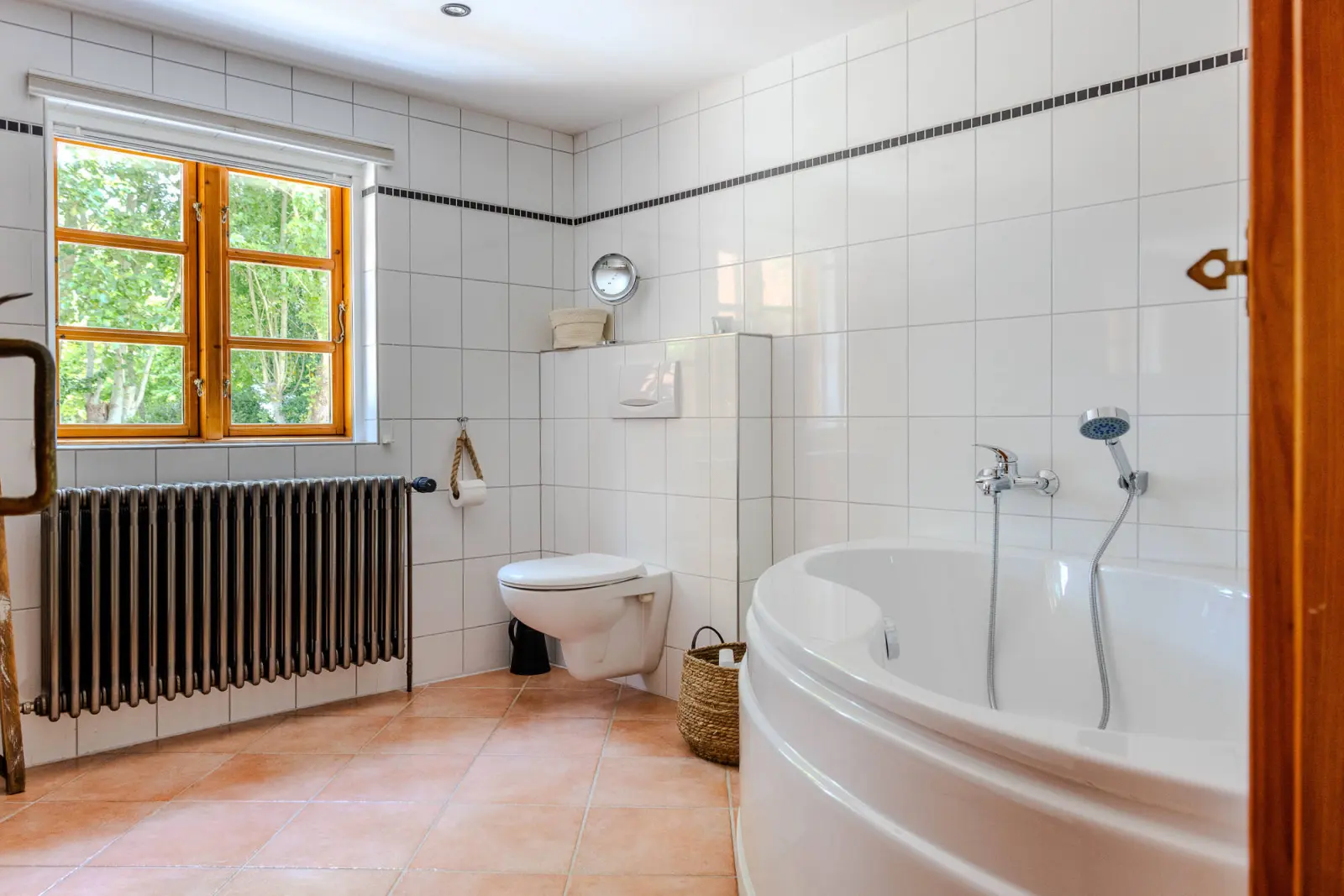 Badezimmer mit weißen Fliesen, Eckbadewanne, Wand-WC und Heizkörper