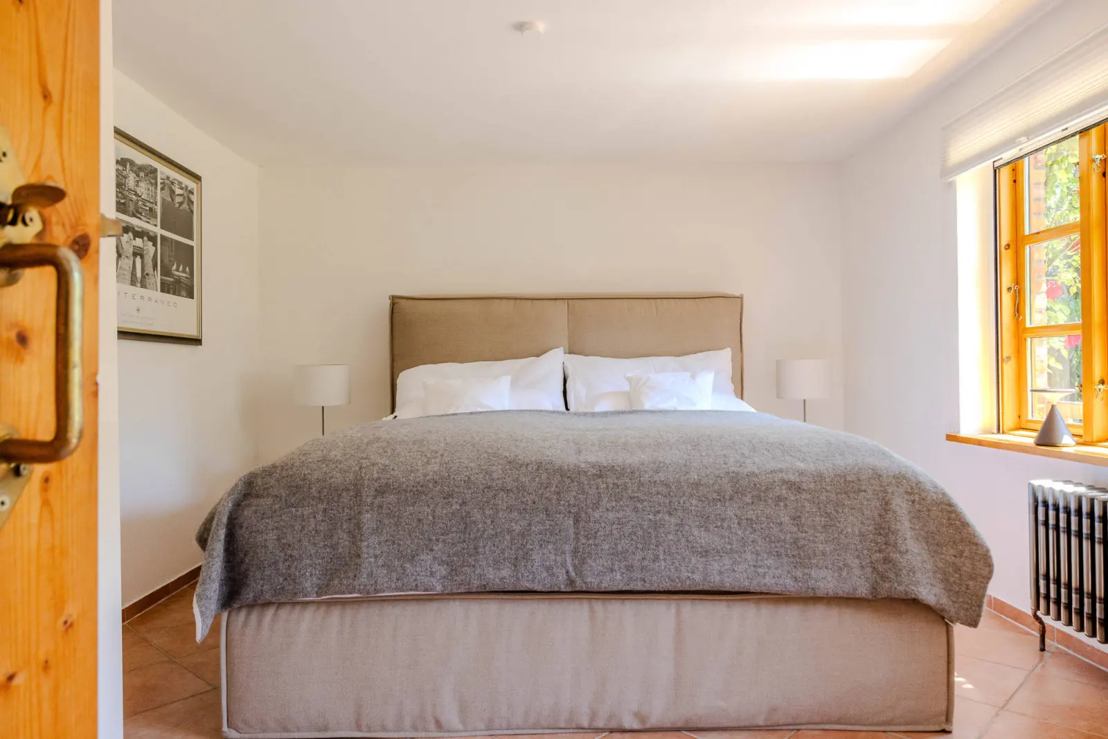 Schlafzimmer mit Doppelbett, grauer Tagesdecke und Fenster mit Holzrahmen