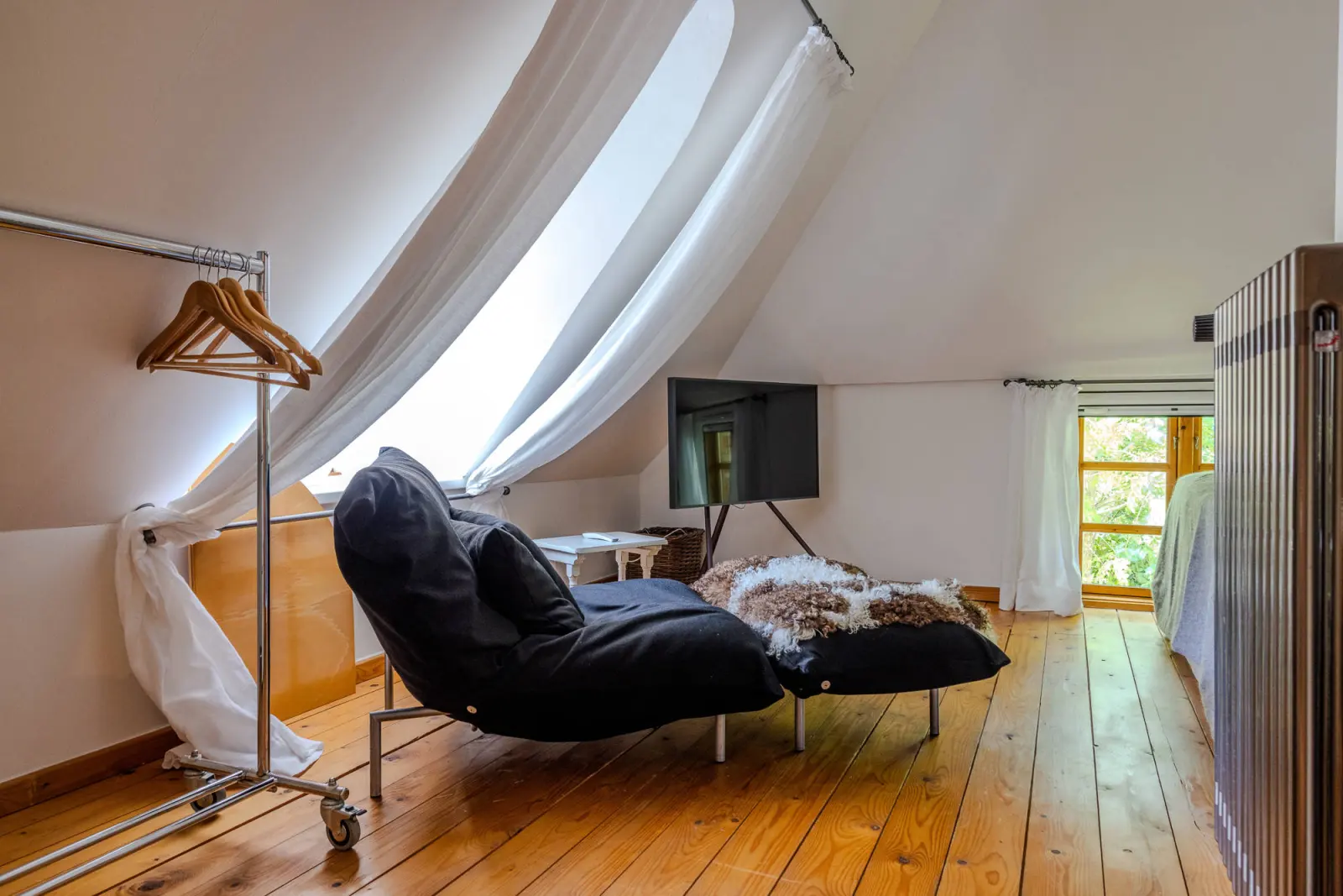 Dachgeschoss mit Liegesessel, Fernseher, Kleiderständer und Vorhang