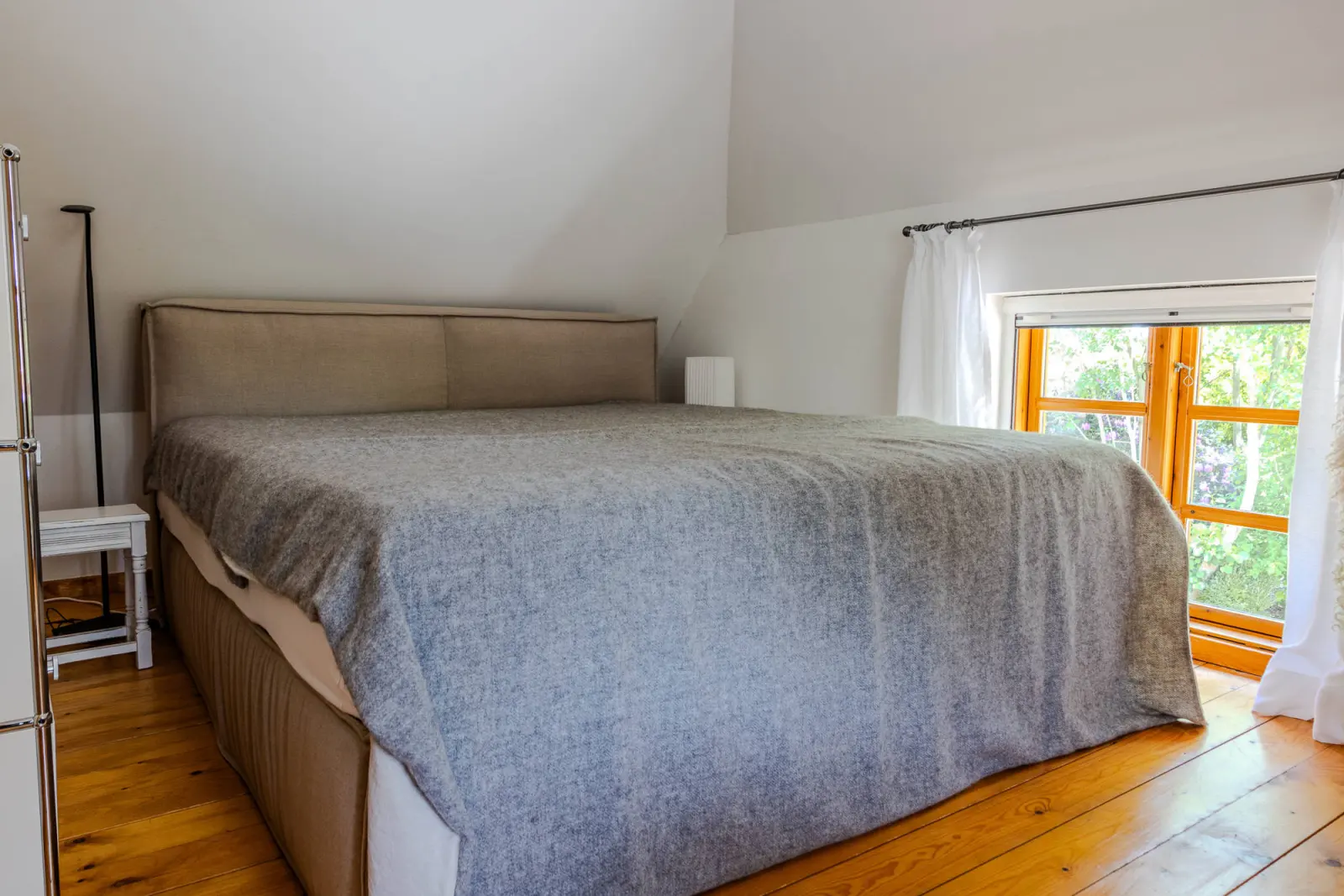 Dachschrägen-Schlafzimmer mit Bett, Rundbogenfenster und Gartenblick