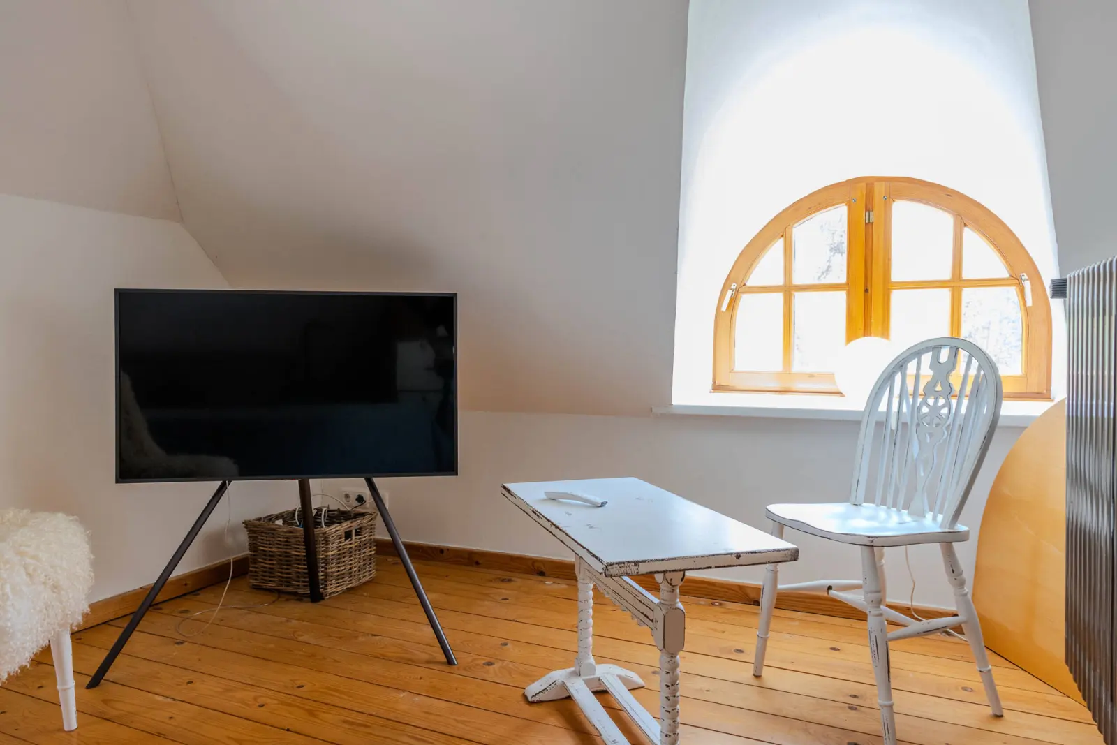 Sitzecke unter der Dachschräge mit Fernseher auf Stativ und Rundbogenfenster