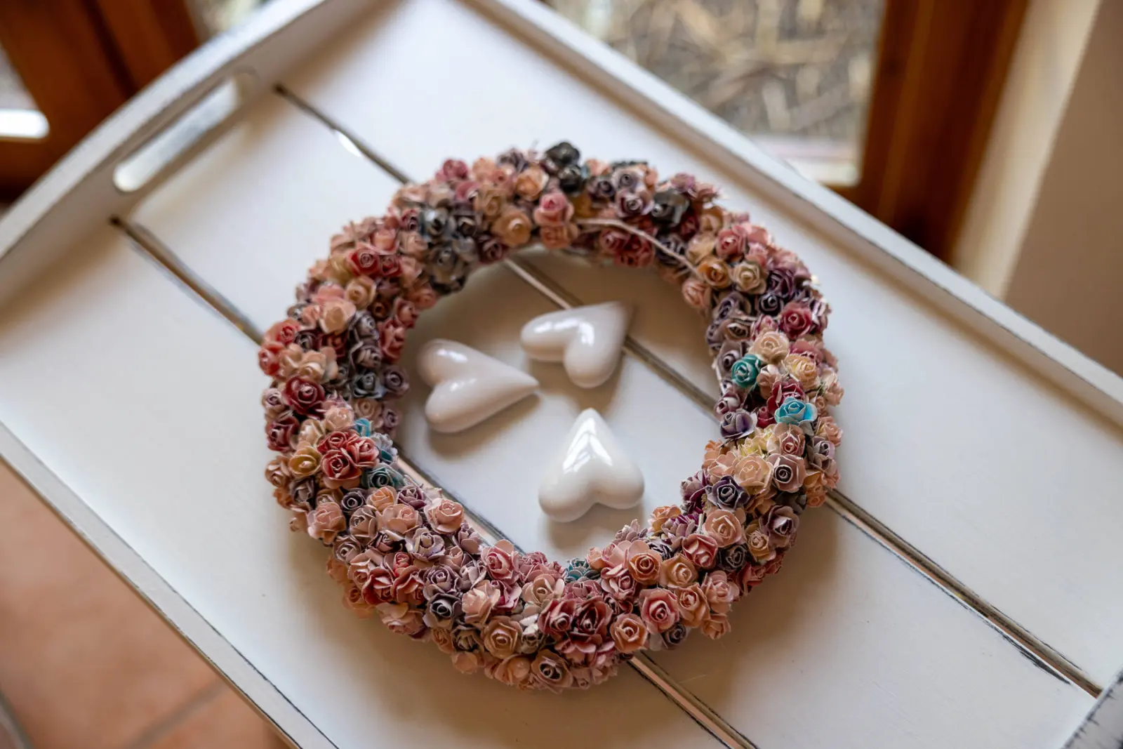 Dekokranz aus Rosenblüten und Porzellanherzen auf einem weißen Tablett