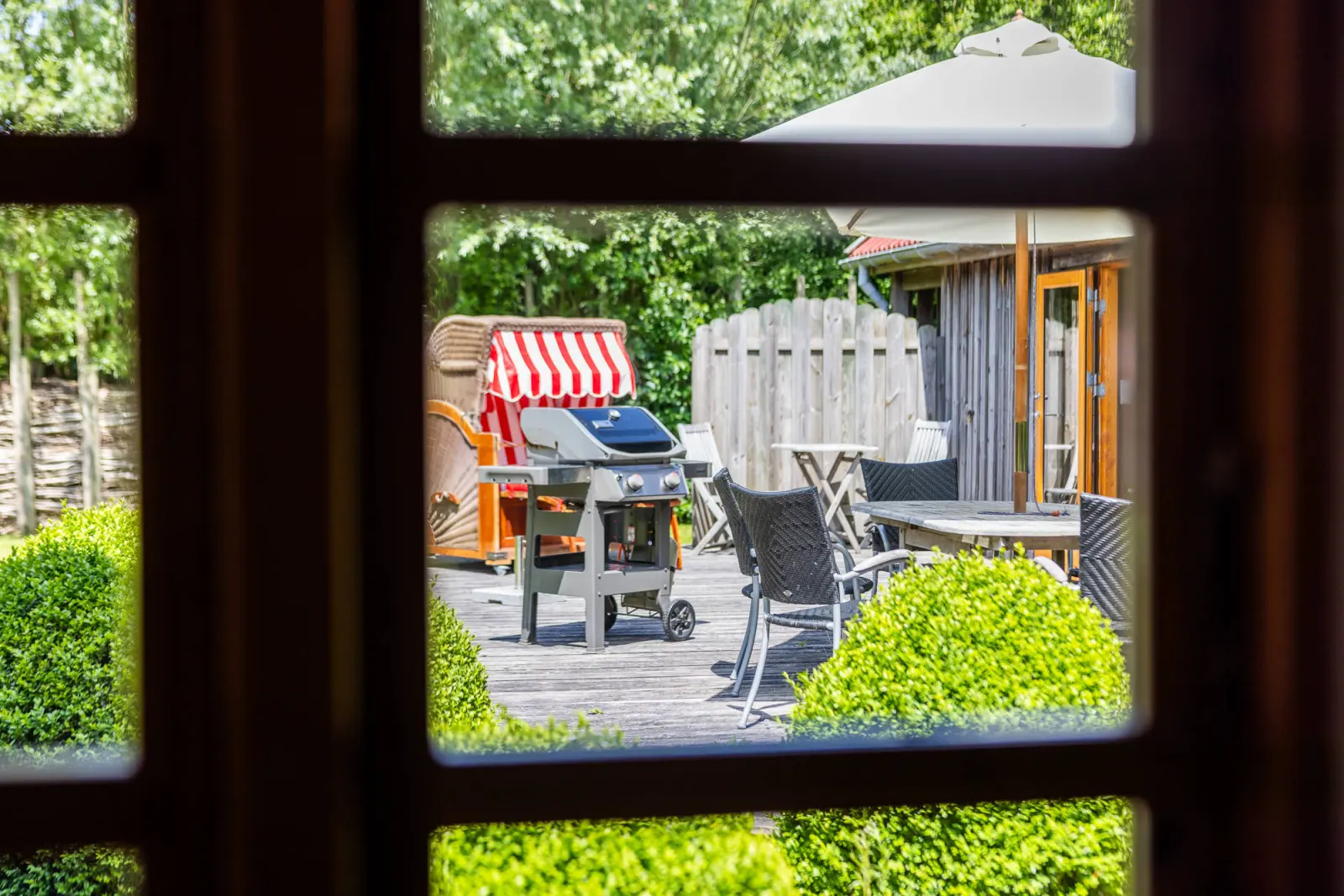 Blick durch das Sprossenfenster auf Strandkorb und Grill auf der Terrasse