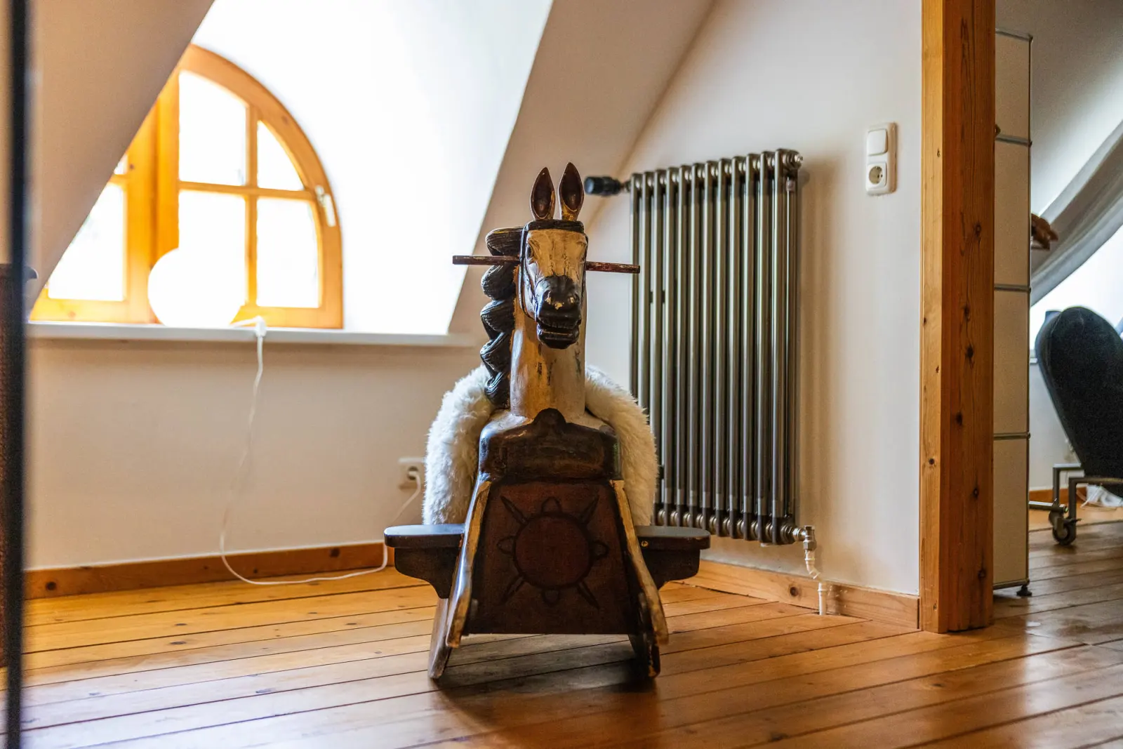 Schaukelpferd mit Fell vor dem Rundbogenfenster und Heizkörper