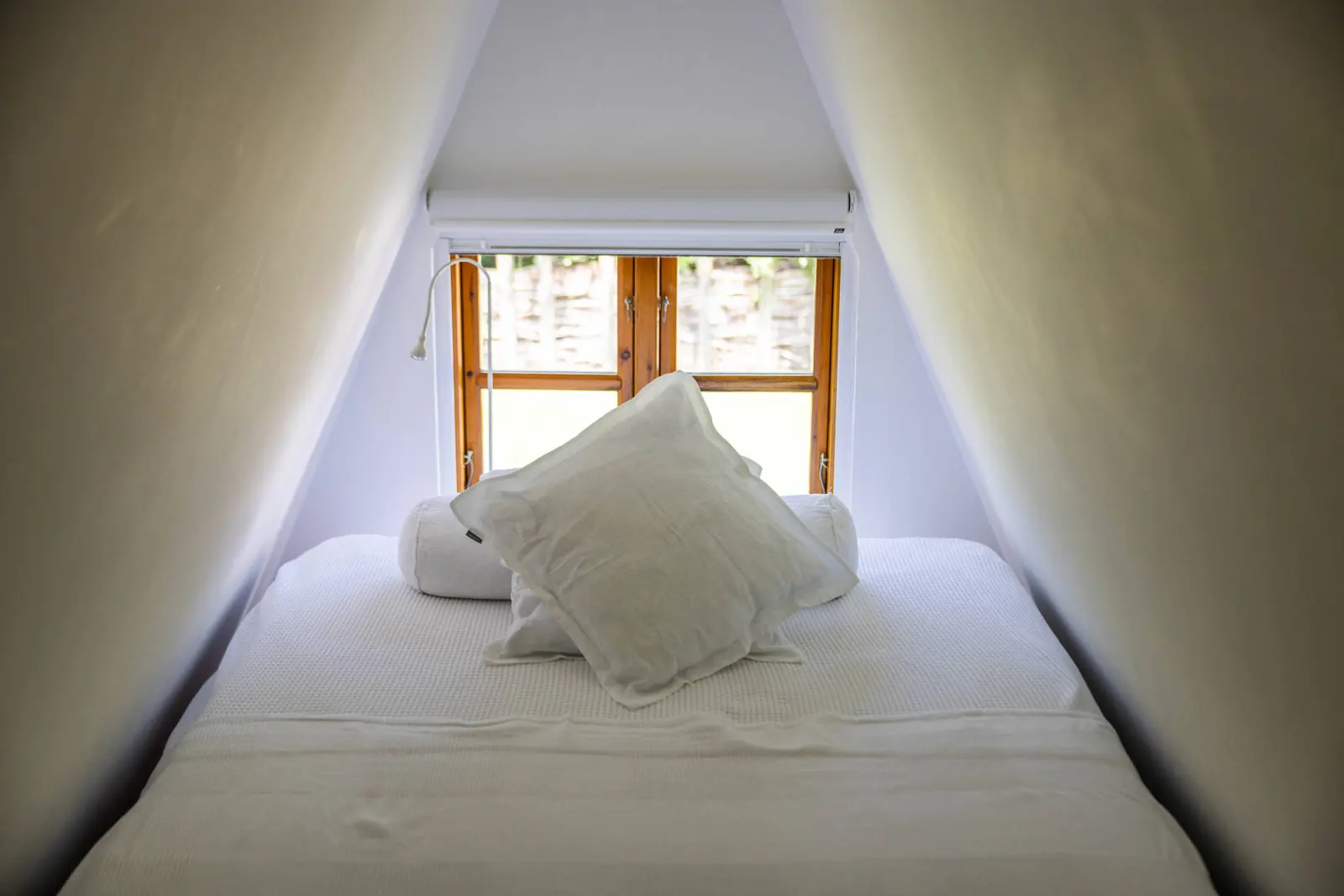 Schmales Bett mit weißen Kissen in der Dachnische, Blick zum Fenster