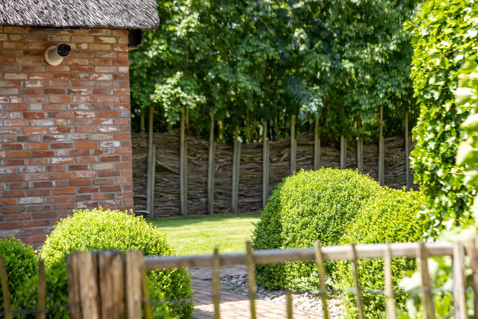 Buchsbaumkugeln und Weidenzaun neben der Backsteinwand im Garten