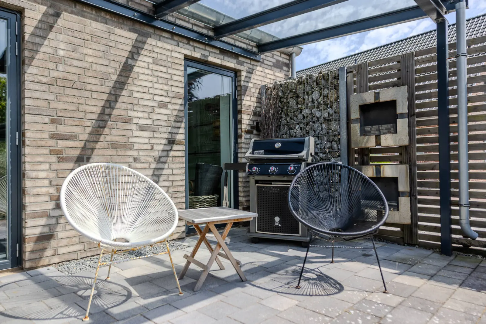 Terrasse mit zwei Acapulco-Stühlen, Gasgrill und Glasüberdachung