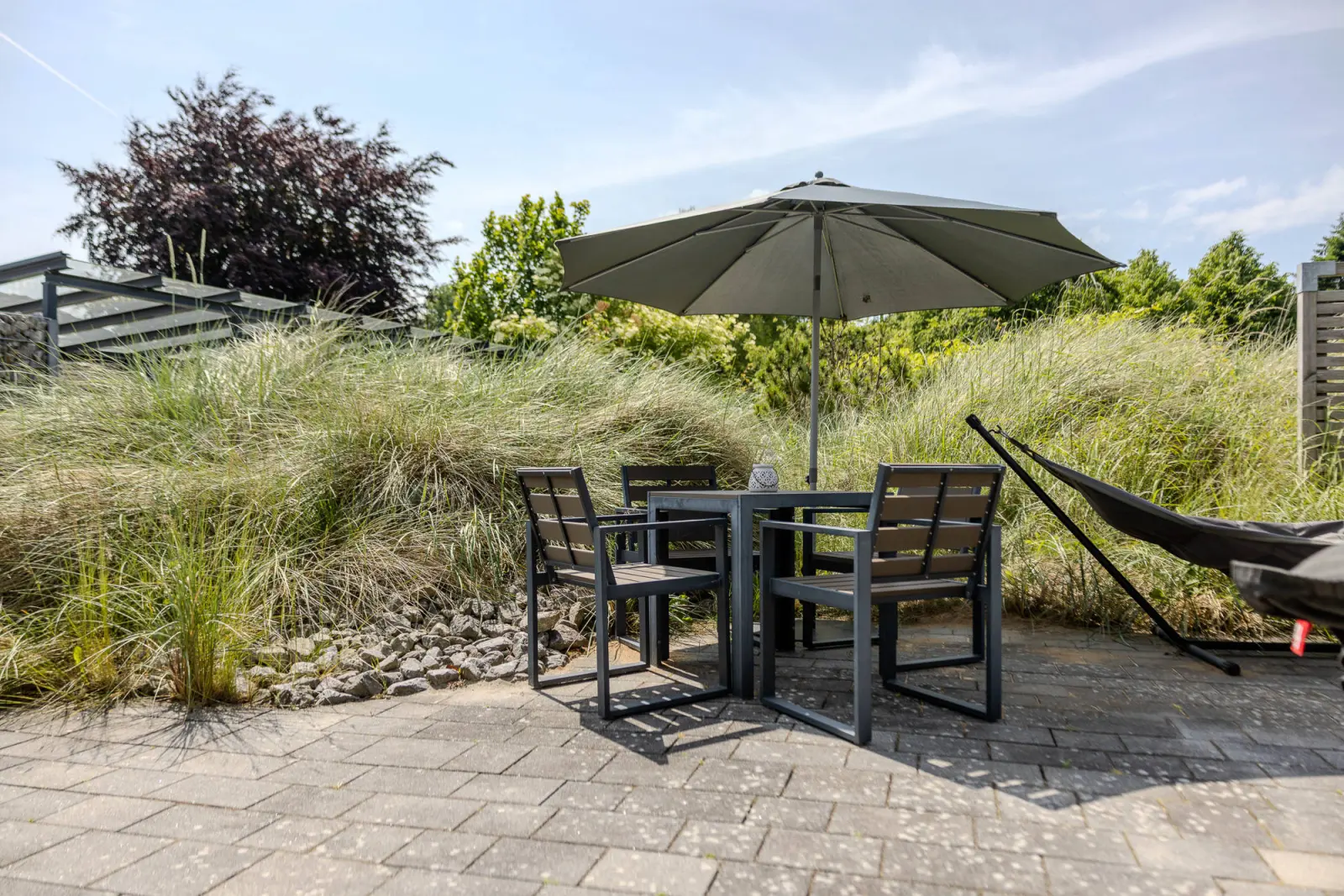 Tisch mit vier Stühlen und Sonnenschirm im Dünengras, Hängematte im Hintergrund