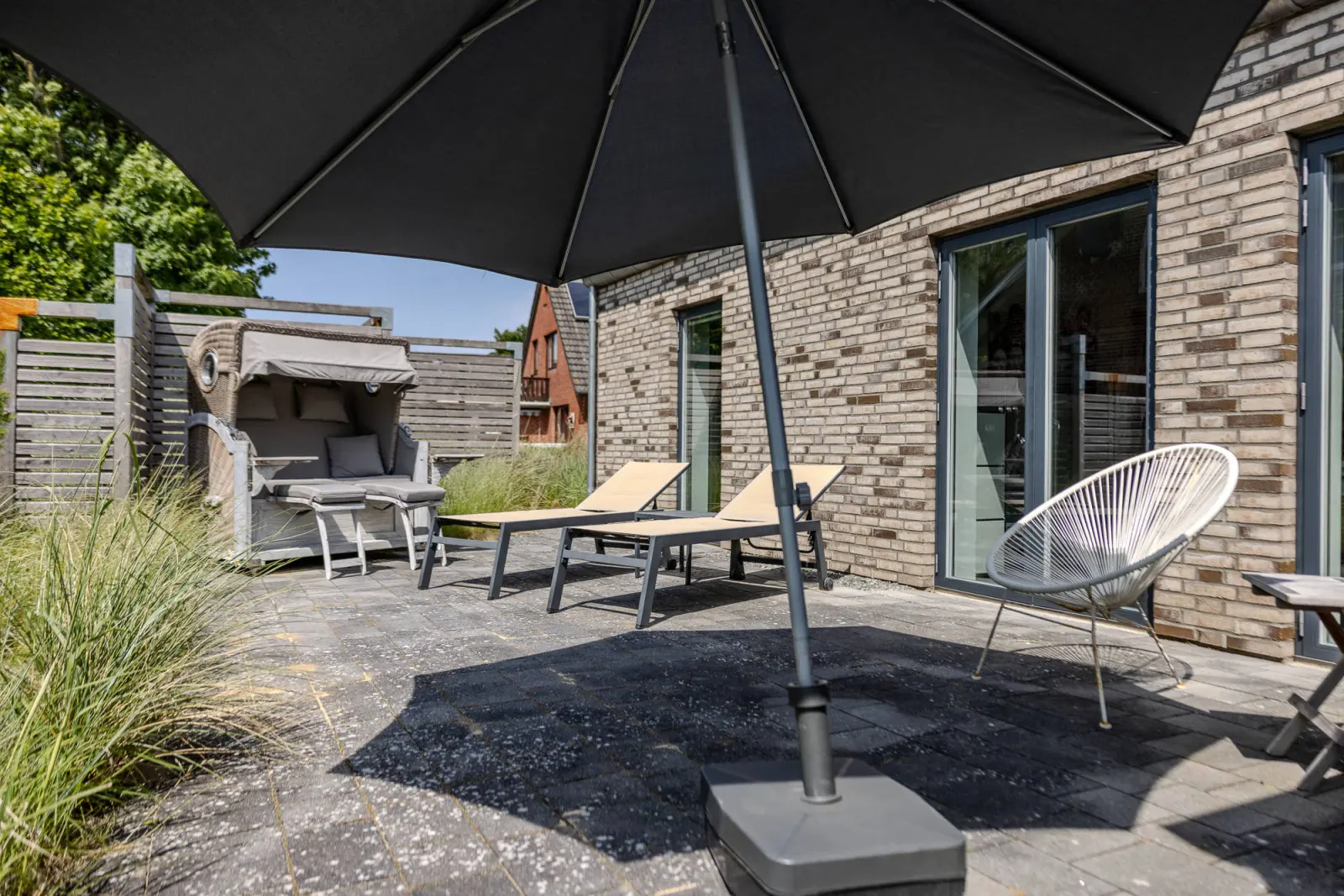 Terrasse mit Sonnenliegen, Strandkorb, Sonnenschirm und Acapulco-Stuhl