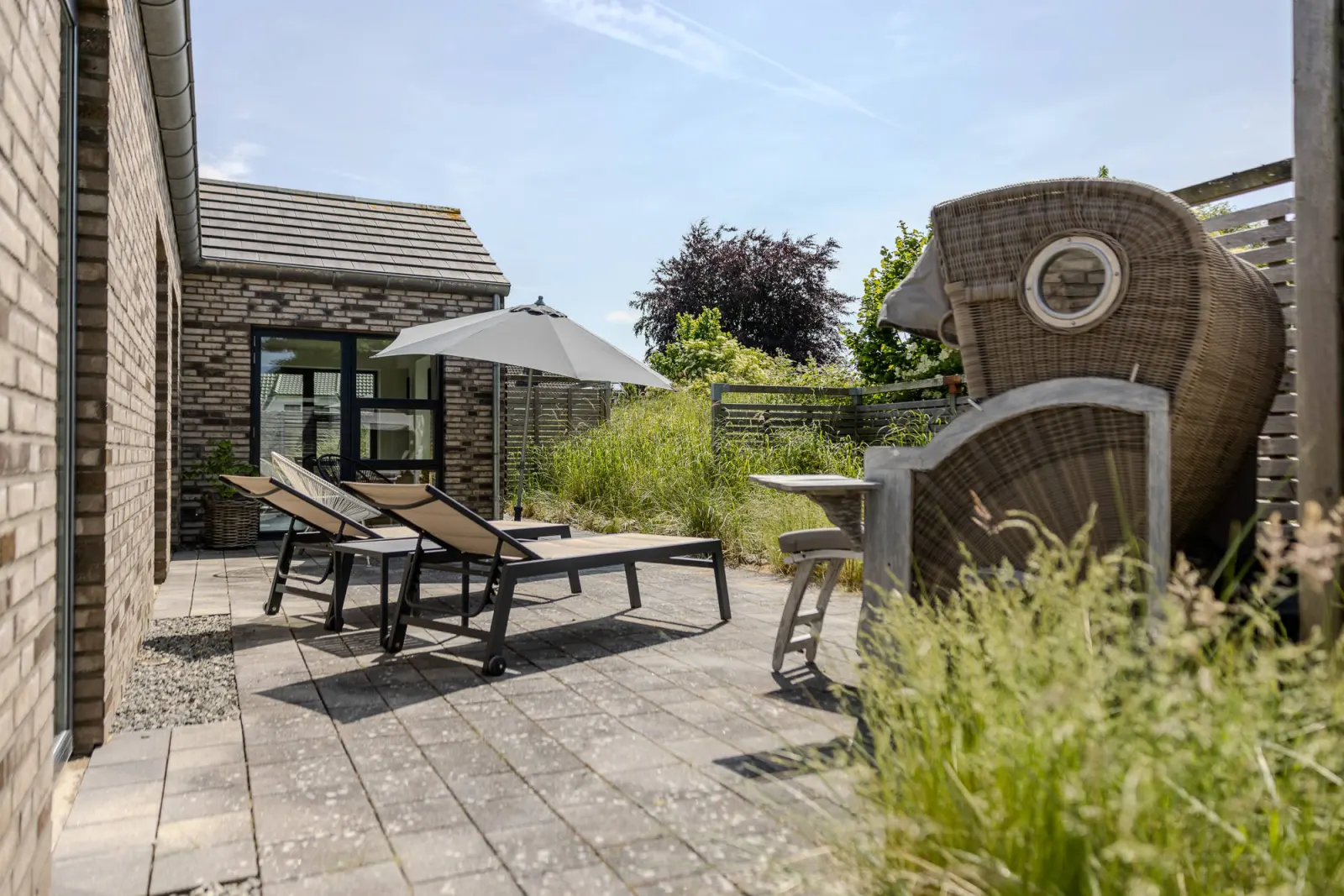 Terrasse mit Sonnenliegen und Rattan-Strandkorb zwischen Gräsern