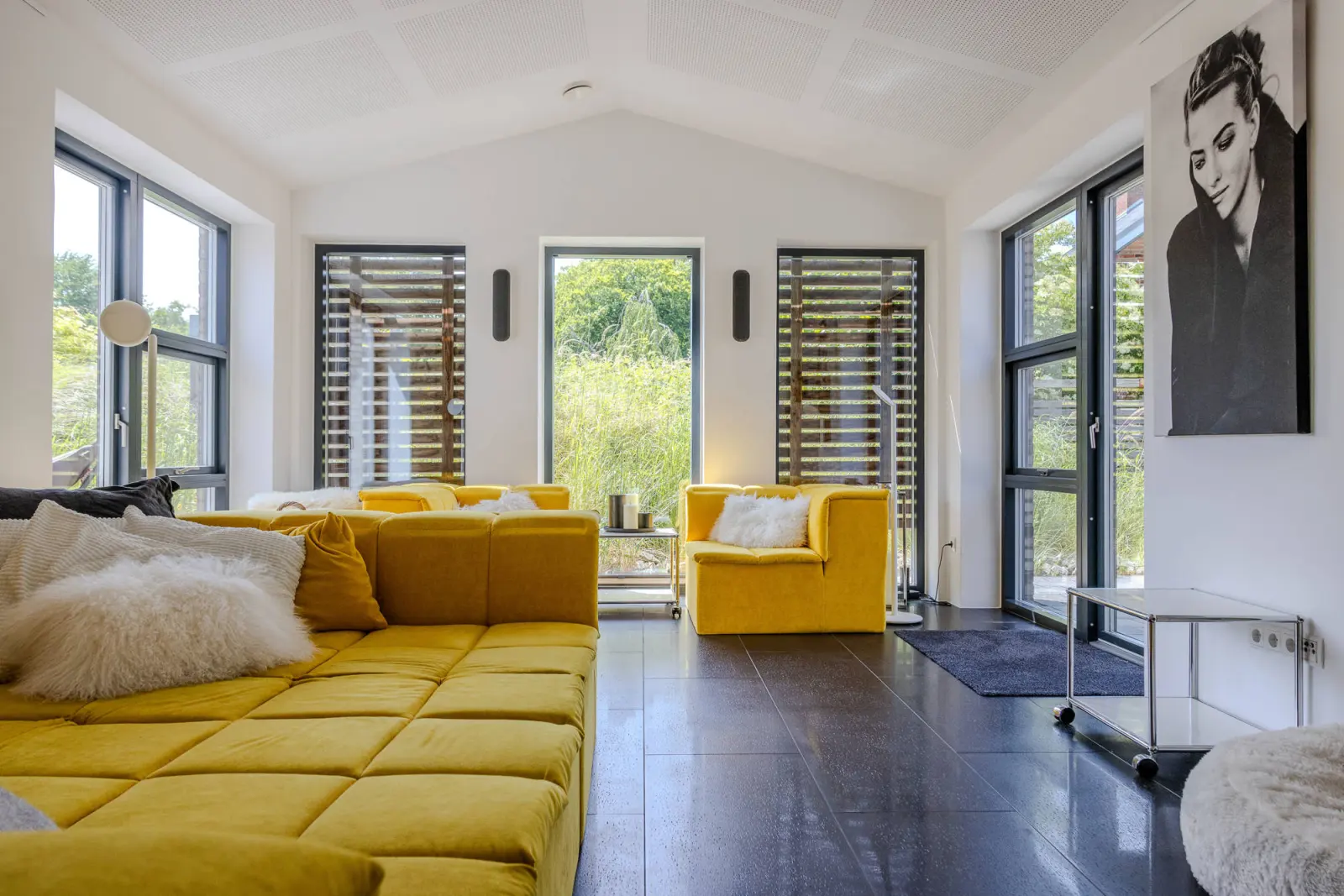 Wohnzimmer mit gelber Sofalandschaft, Fellkissen und großem Fensterfront