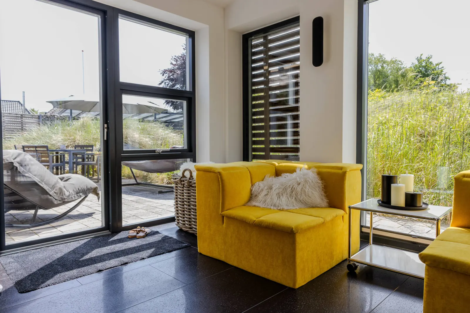 Terrassentür mit Holzlamellen, gelber Sessel und Blick auf die Terrasse