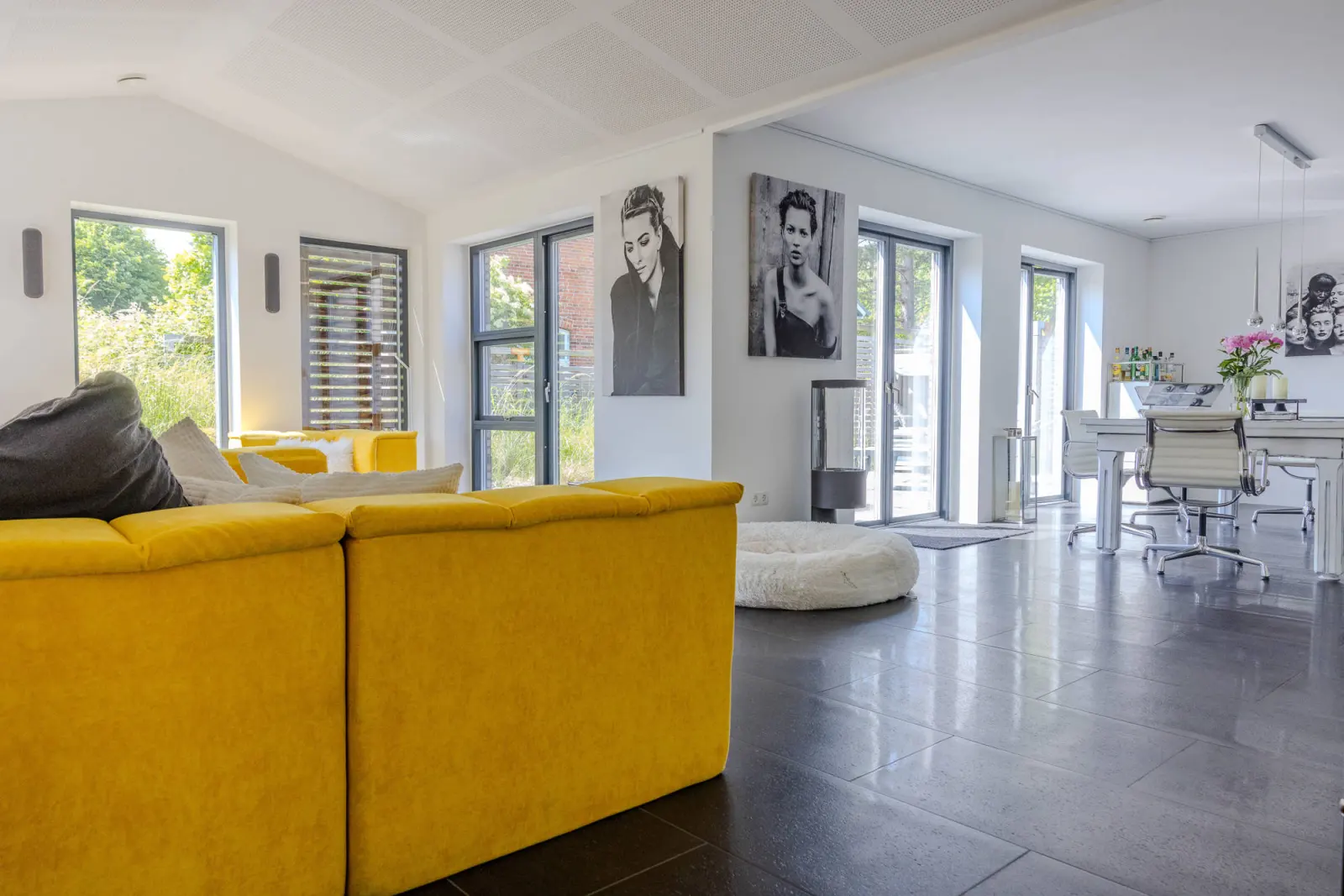 Offener Wohnraum mit gelbem Sofa, Kaminofen und Esstisch im Hintergrund
