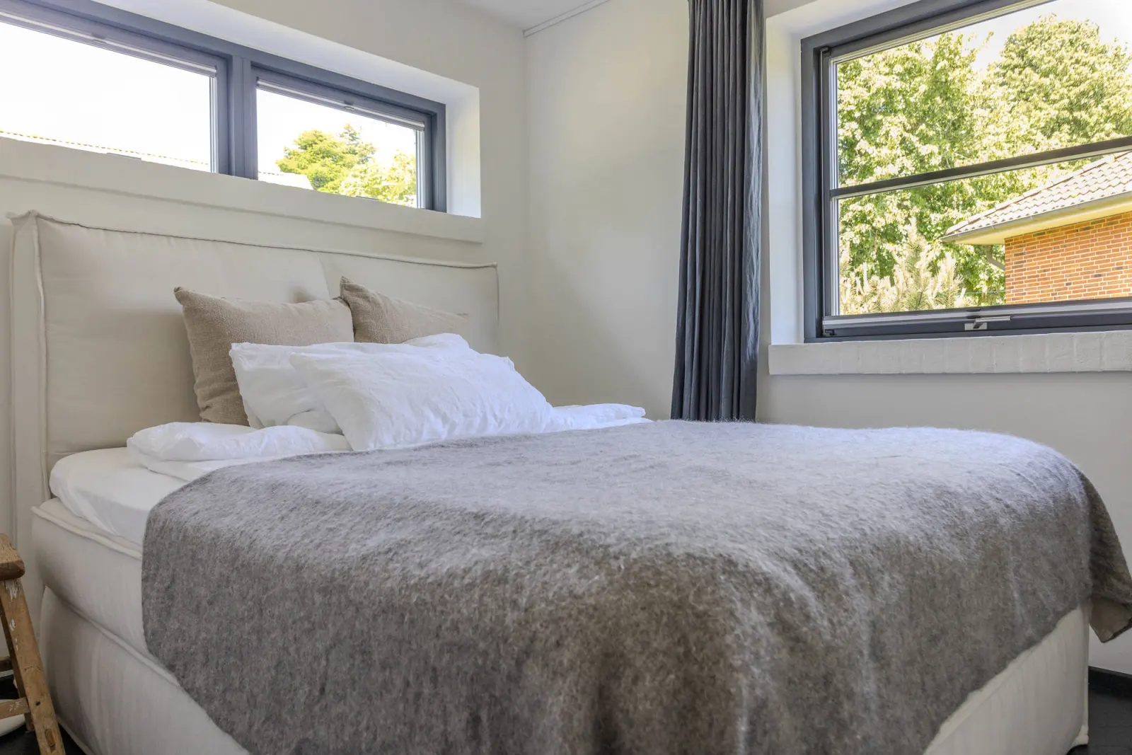 Bett mit Kissen und grauer Decke vor Fenstern im Schlafzimmer