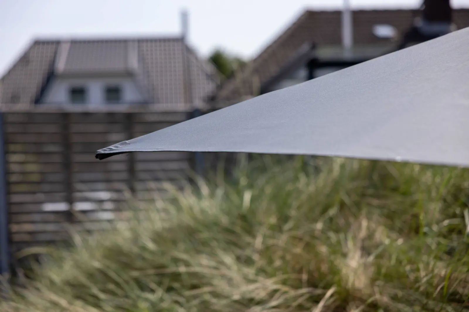 Sonnenschirm und Dünengras vor Holzzaun, Detail der Terrasse