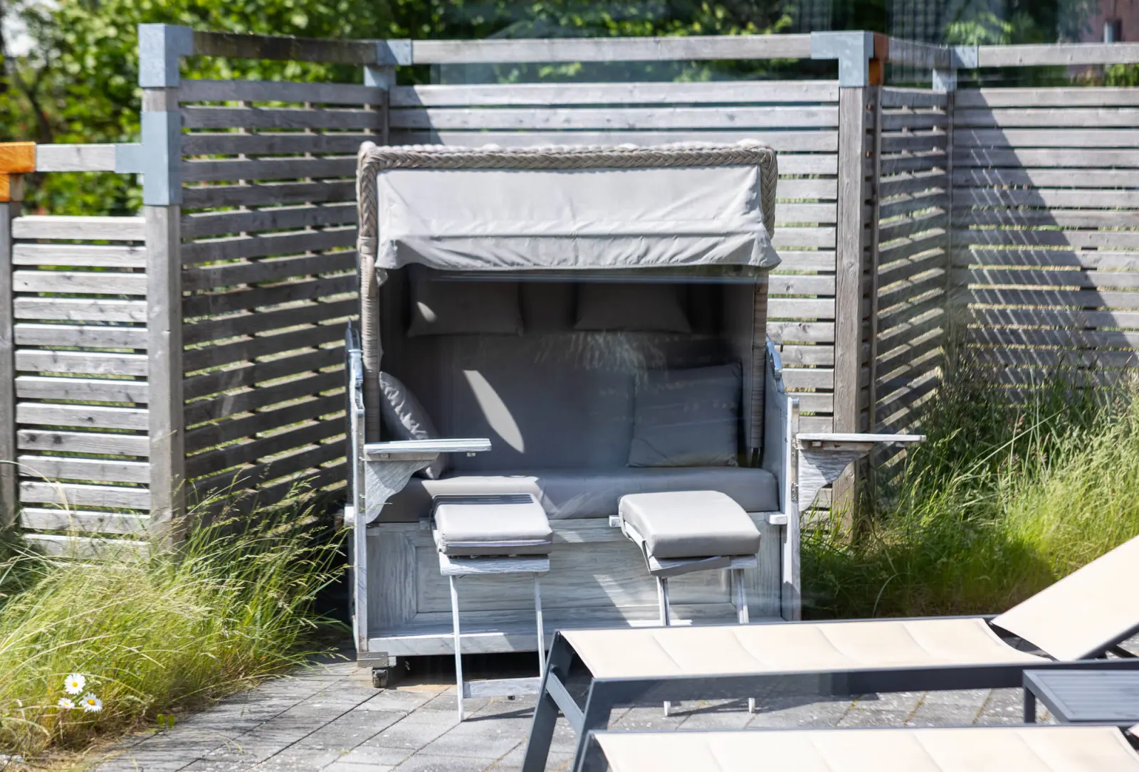 Strandkorb mit Fußhockern und Sonnenliege vor Holzsichtschutz