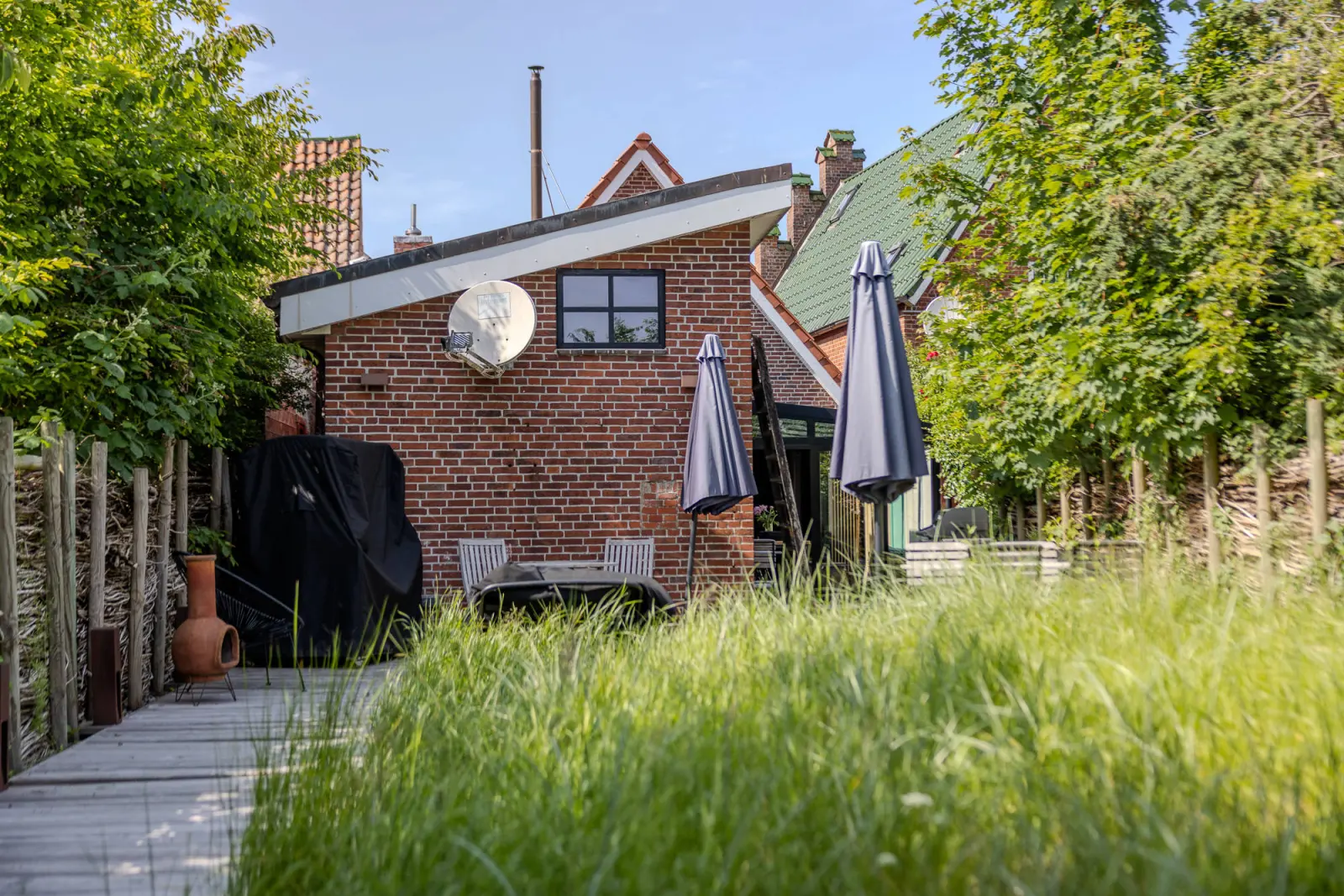 Rückseite des Stadthauses mit Garten, Sonnenschirmen und Weidenzaun im Gras