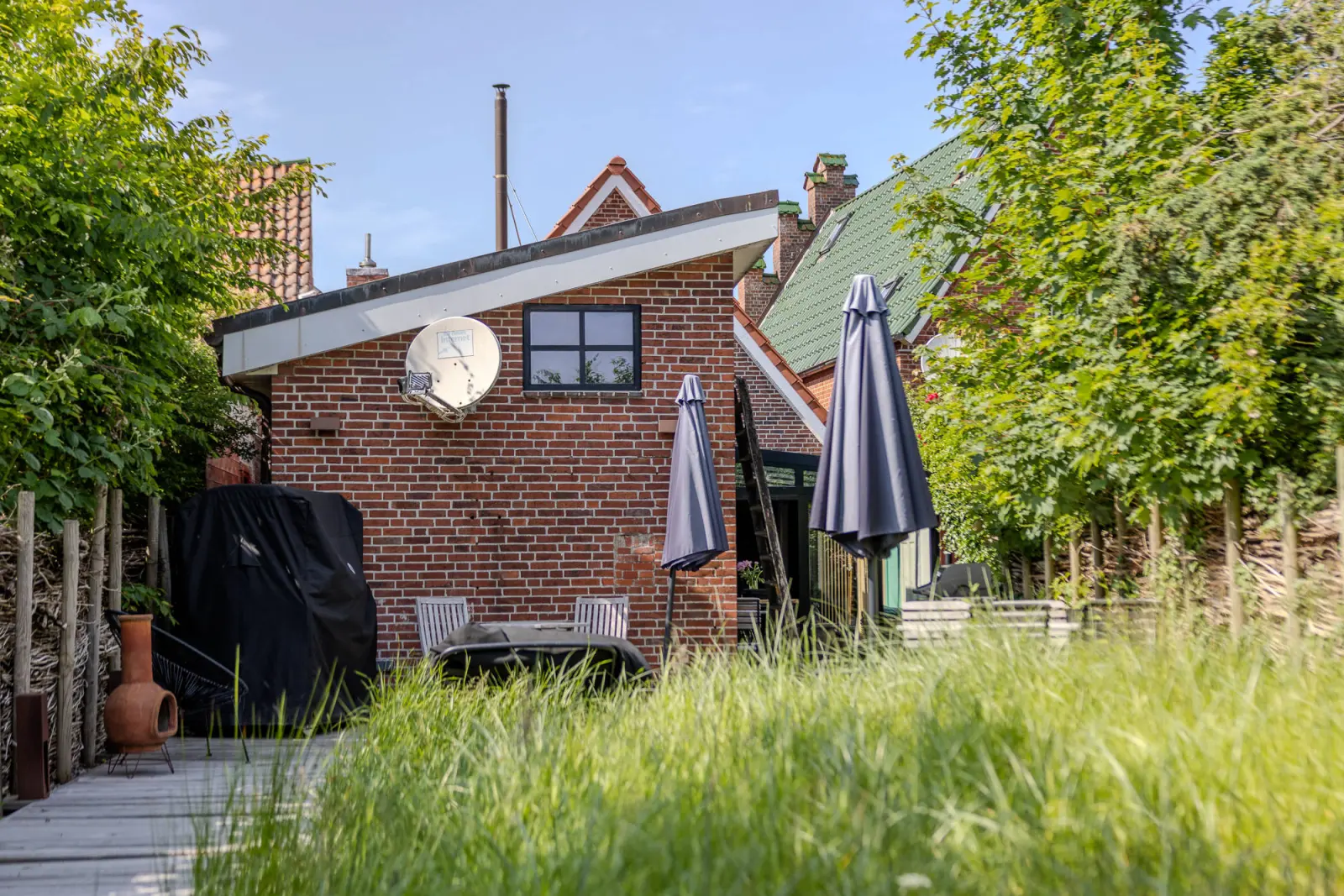 Backsteinanbau mit Satellitenschüssel, Grill und hohem Gras im Stadtgarten