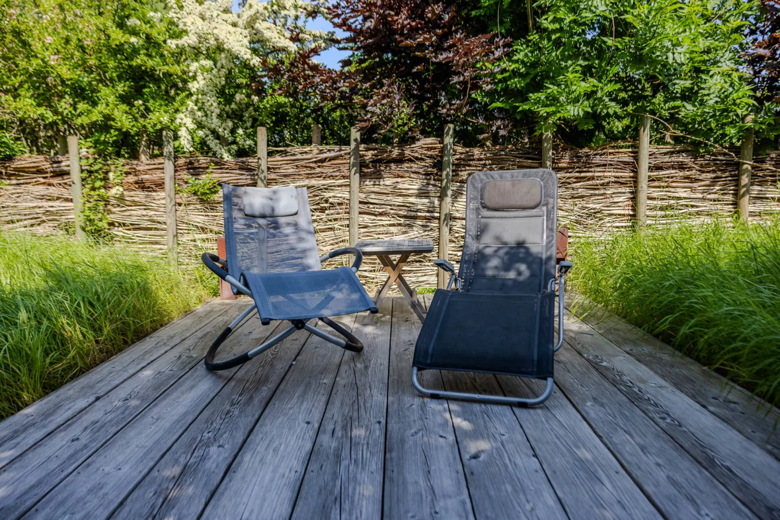 Zwei Relaxliegen auf der Holzterrasse vor Weidenzaun und Ziergräsern