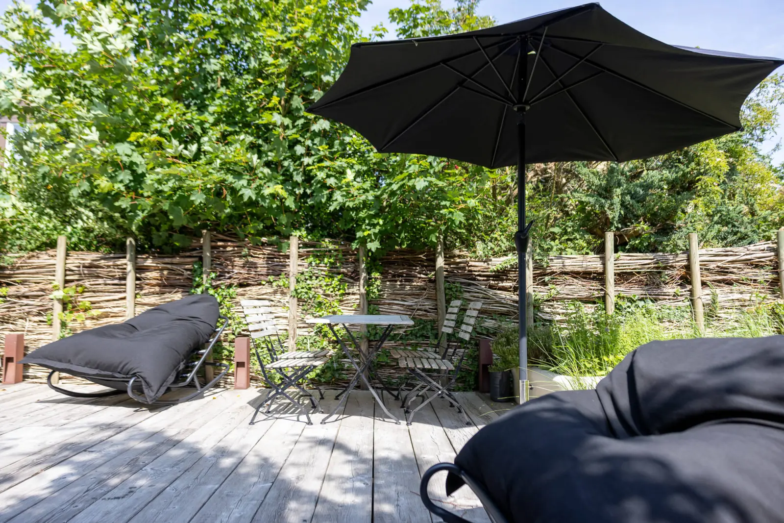 Gartenterrasse mit großem Sonnenschirm, Klappstühlen und Sitzsäcken im Grünen