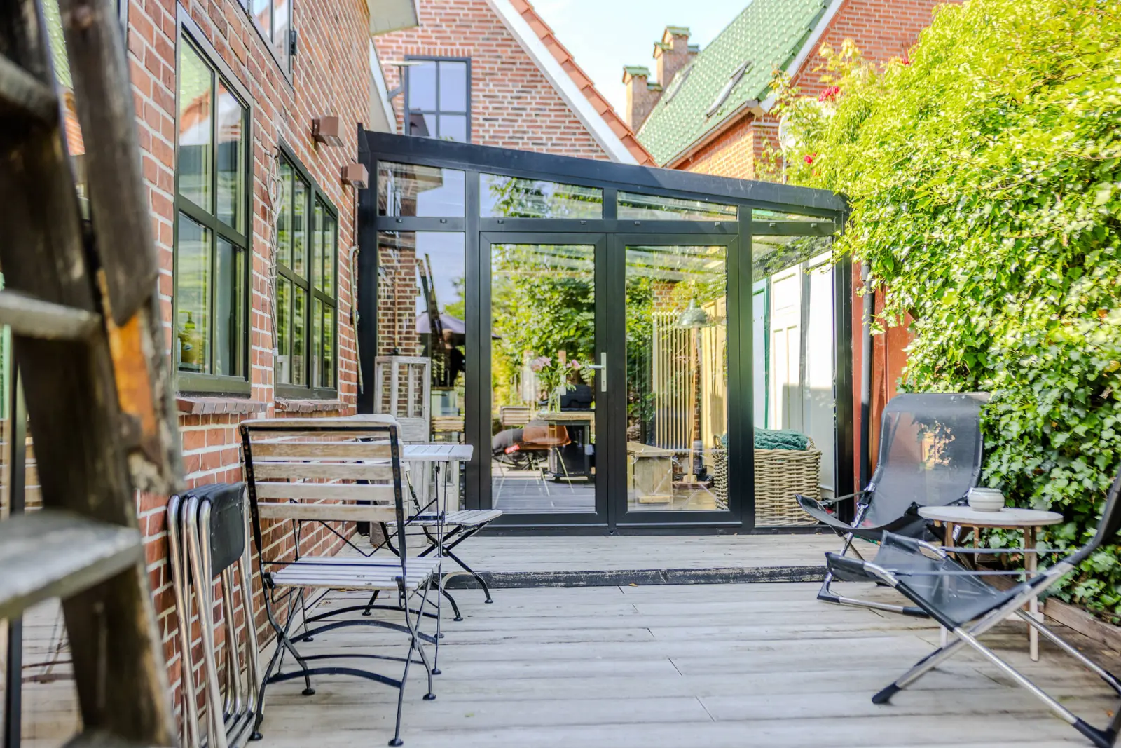 Glasanbau mit Terrassentür, Klappstühlen und Liegestuhl auf der Holzterrasse