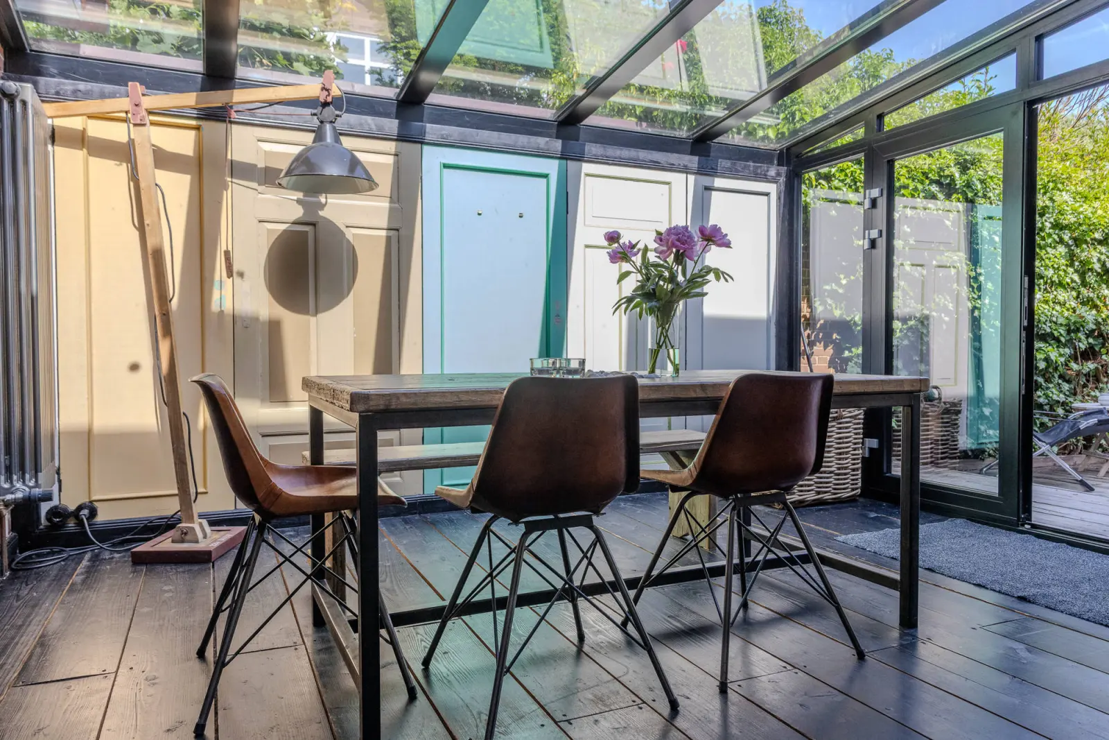 Esstisch mit Lederstühlen im Wintergarten mit Blumenstrauß und bunten Türen