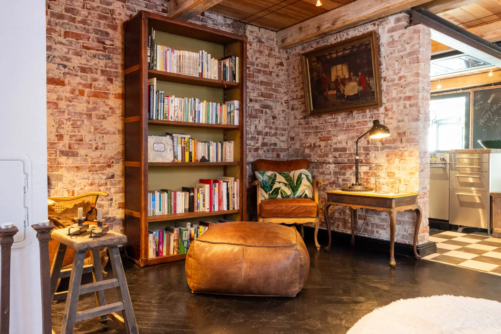Bücherregal, Beistelltisch und Sessel mit Pouf vor sichtbarer Backsteinwand