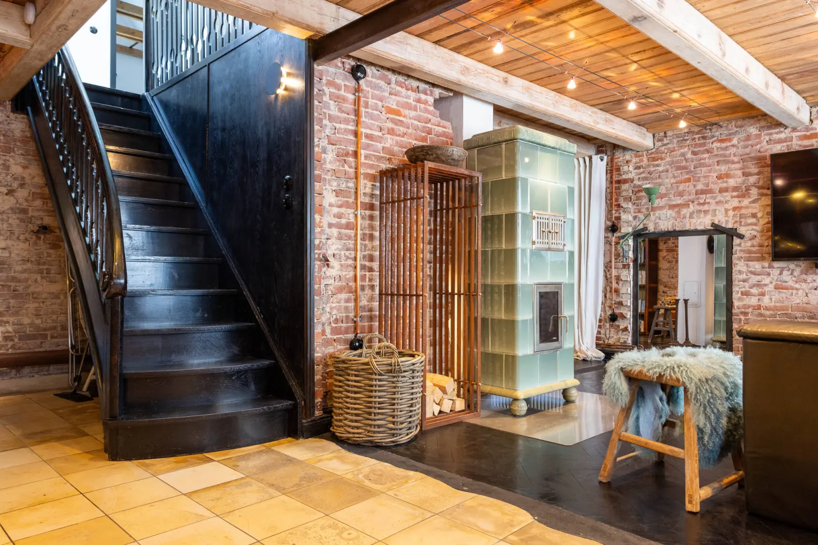 Diele mit schwarzer Treppe, grünem Kachelofen und Fellhocker