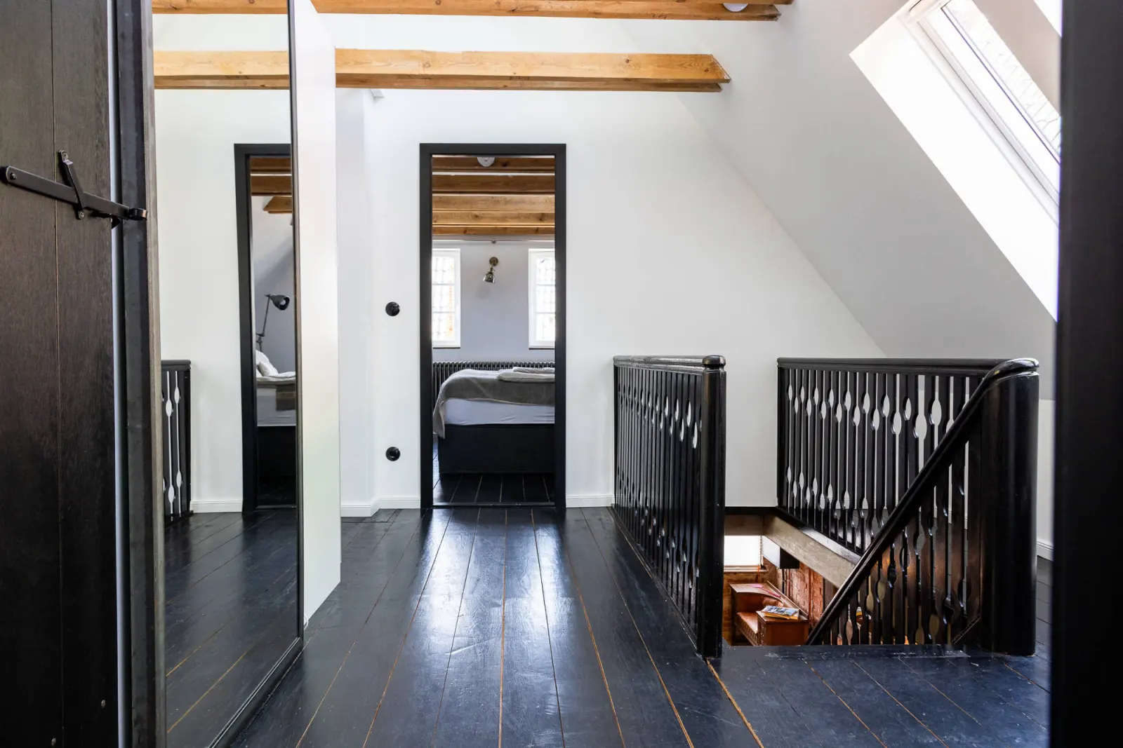 Obergeschoss-Flur mit schwarzem Dielenboden, Treppengeländer und Schlafzimmer im Hintergrund