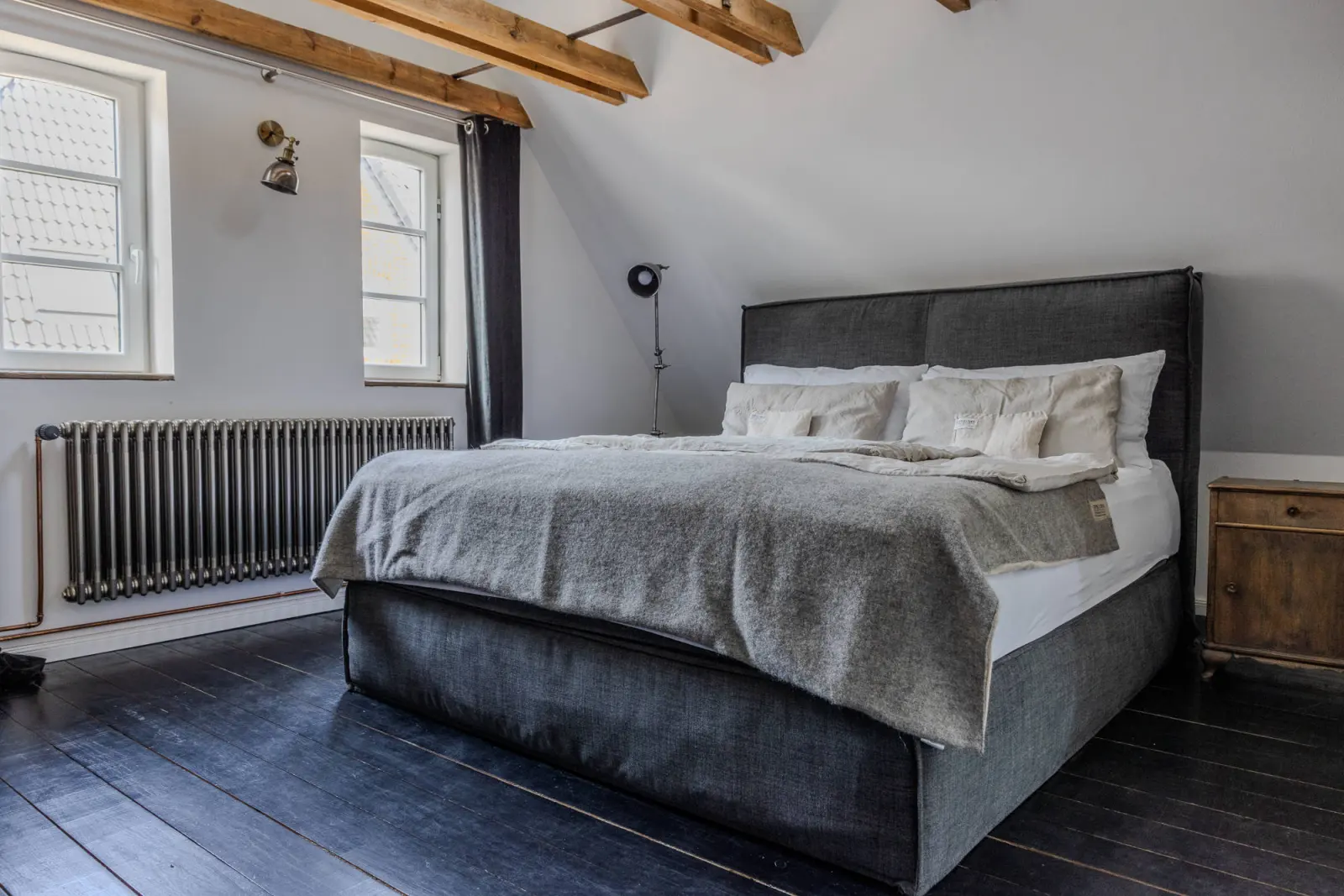 Doppelbett mit grauer Decke, Sprossenfenstern und Holzbalken im Dachgeschoss