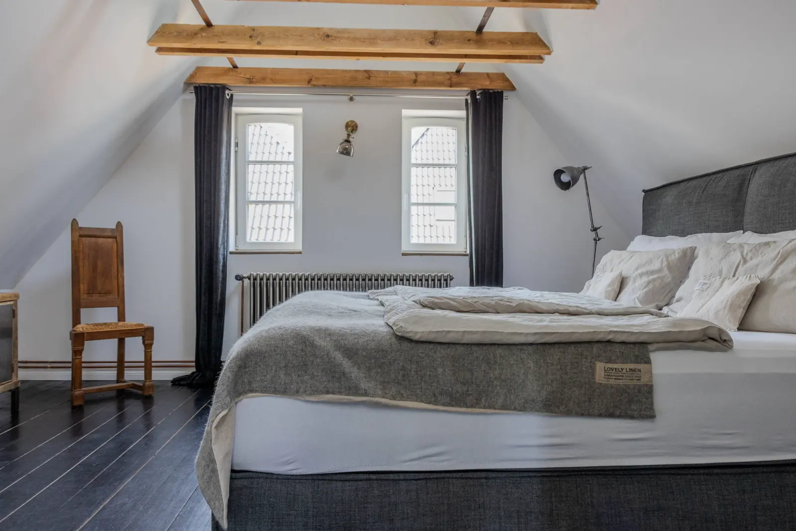Schlafzimmer mit Boxspringbett, Holzstuhl und Heizkörper unter Sichtbalken
