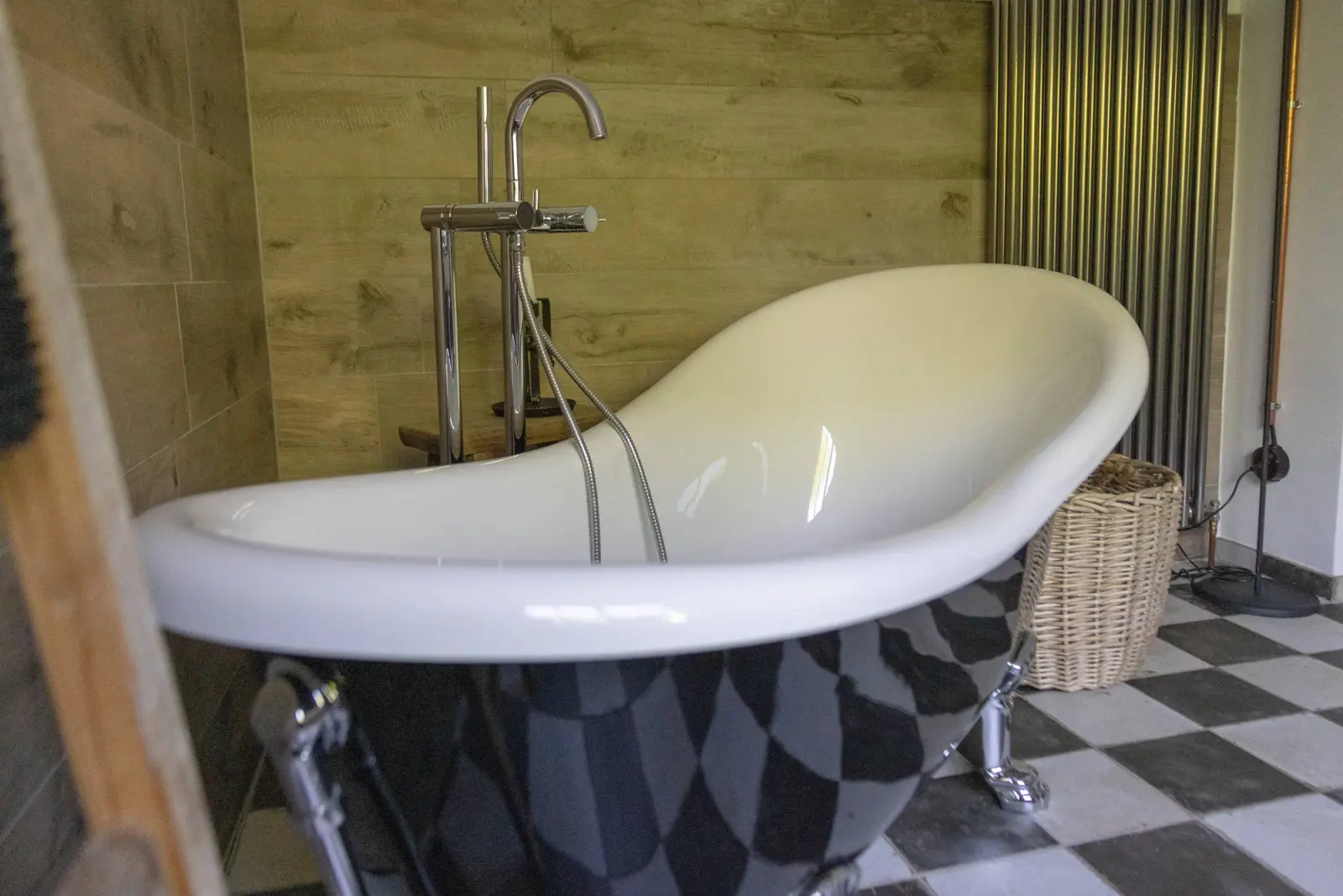 Badewanne auf Löwenfüßen mit Armatur und Korb vor Holzwand