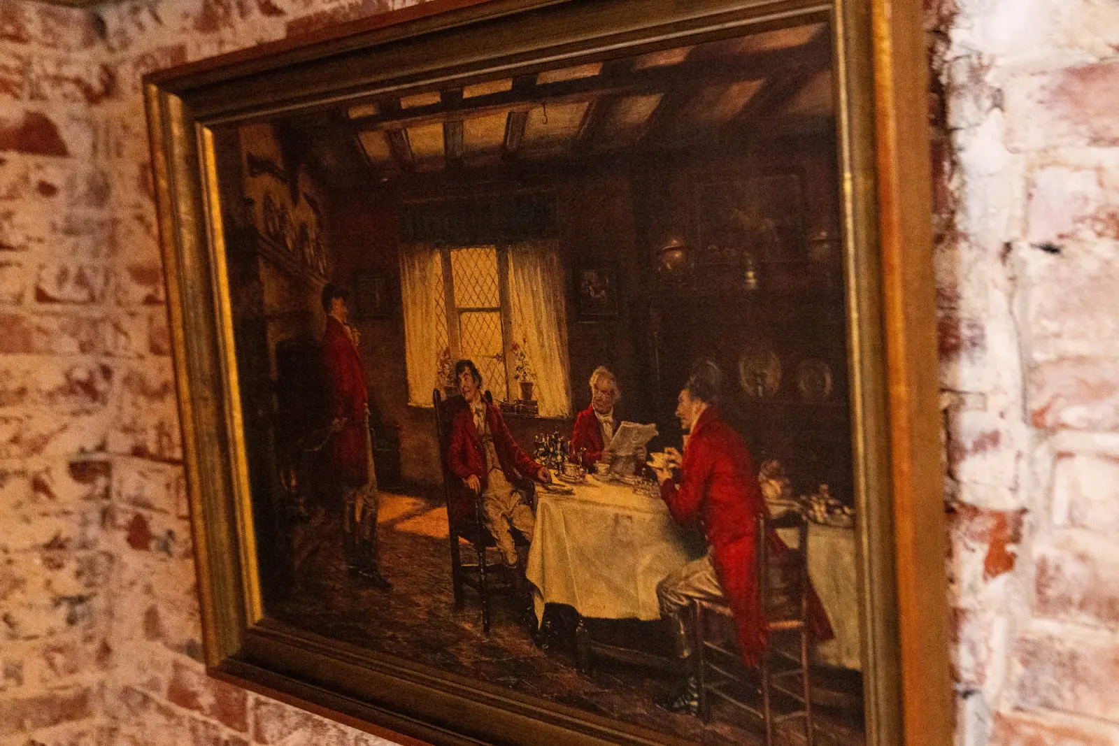 Gemälde mit Tischgesellschaft im goldenen Rahmen an der Backsteinwand