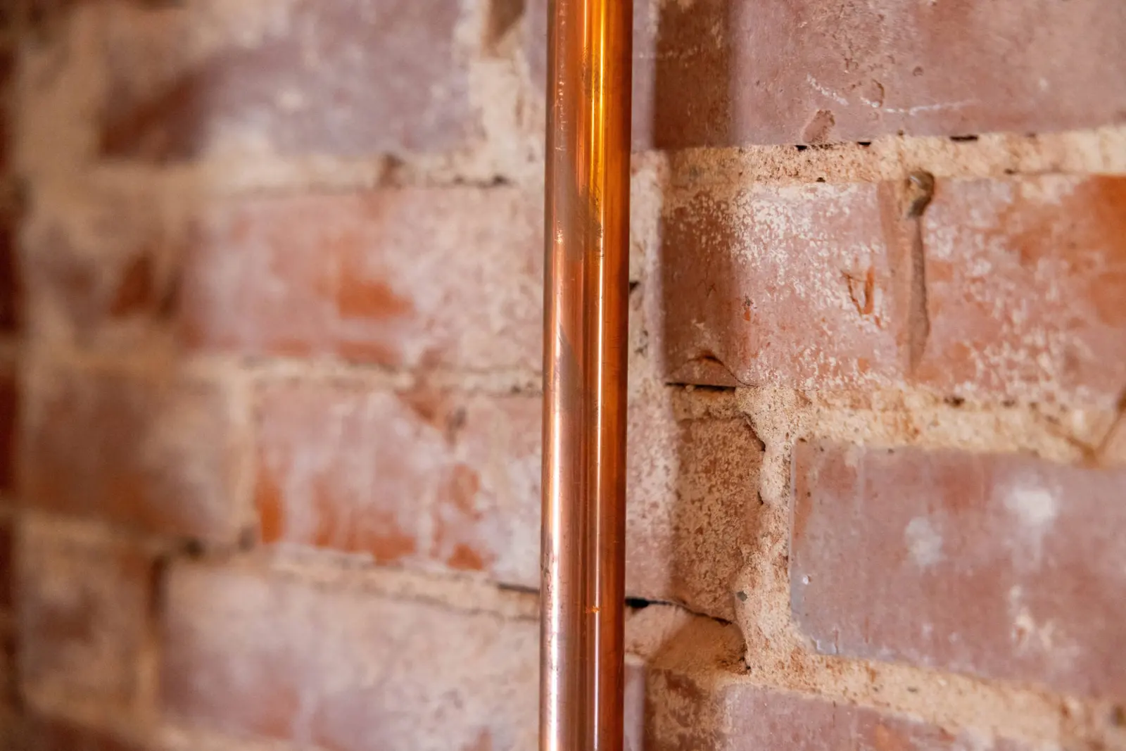 Backsteinwand mit Kupferrohr, Detailaufnahme