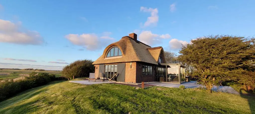 Landhaus auf der Warft mit Rasen, Terrasse und Blick über die Marsch im Sonnenlicht
