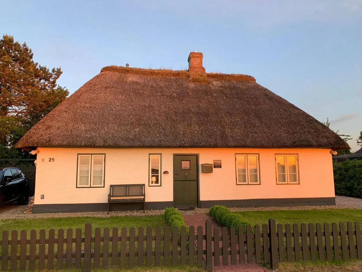 Reetdachkate in warmem Abendlicht mit Lattenzaun und Gartenbank