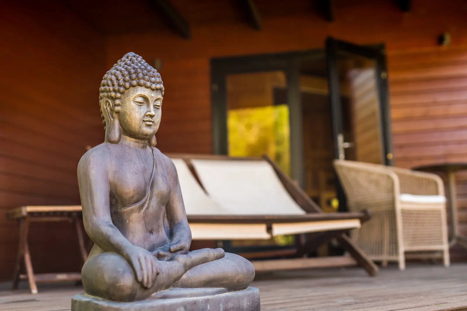 Buddha-Statue und Liegestuhl auf der überdachten Holzterrasse am Saunahaus
