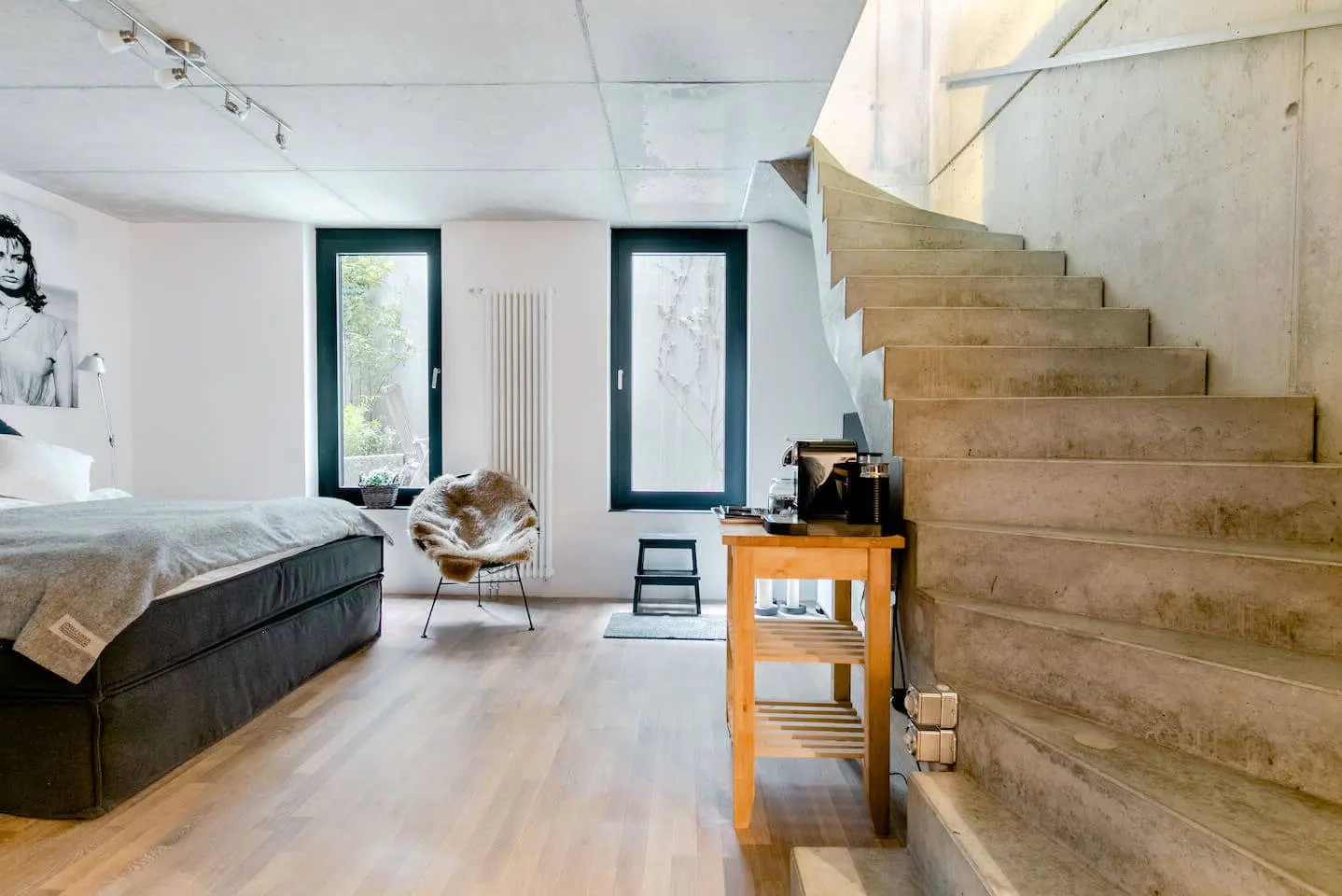 Betonwendel-Treppe, Fernsehecke und Doppelbett mit grauer Tagesdecke im Loft