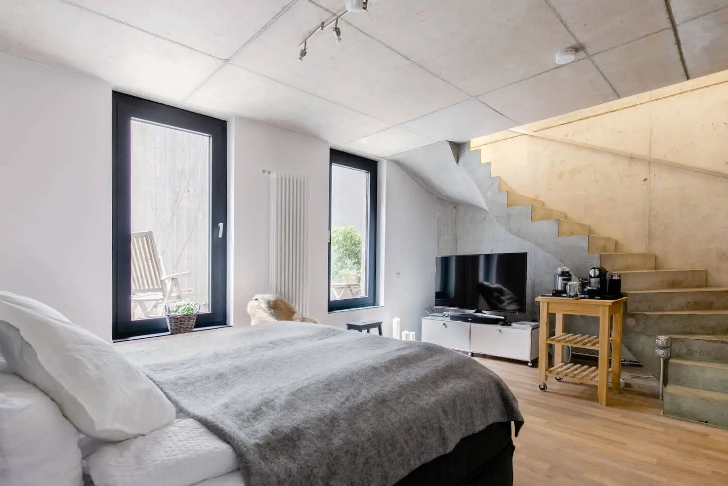 Schlafbereich mit Boxspringbett, Fernseher und frei tragender Betontreppe
