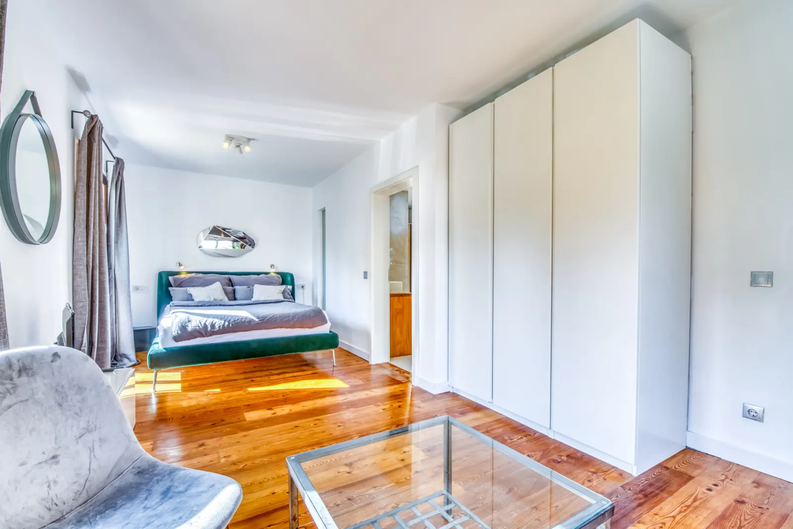Schlafzimmer mit grünem Bett, Sitzecke, Glastisch und weißem Kleiderschrank