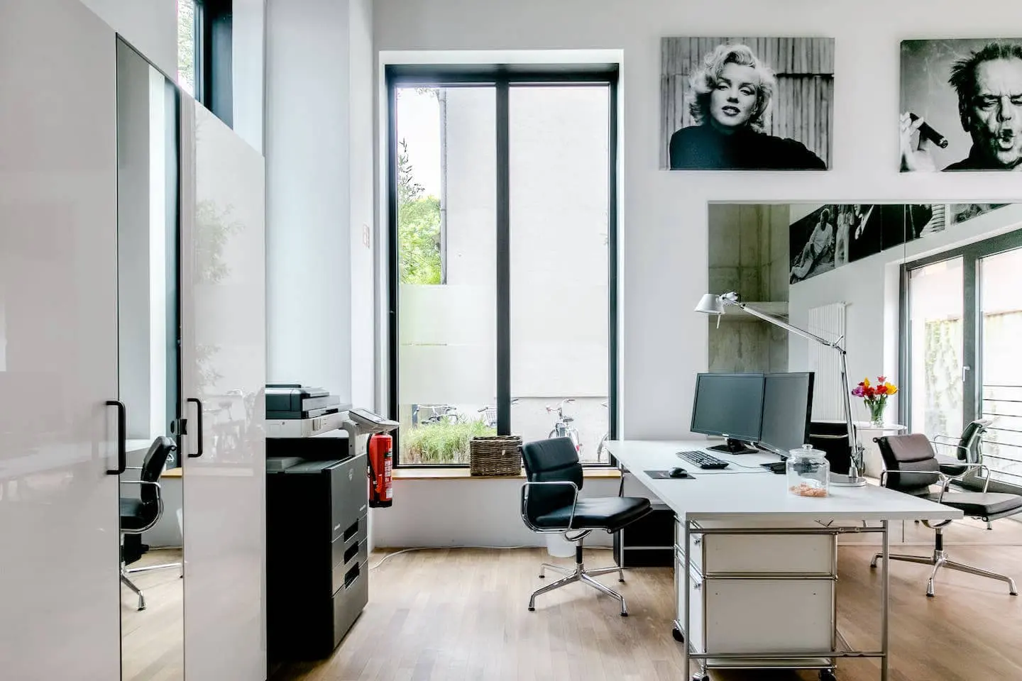 Büroecke mit Schreibtisch und Bürostühlen vor bodentiefen Fenstern im Loft